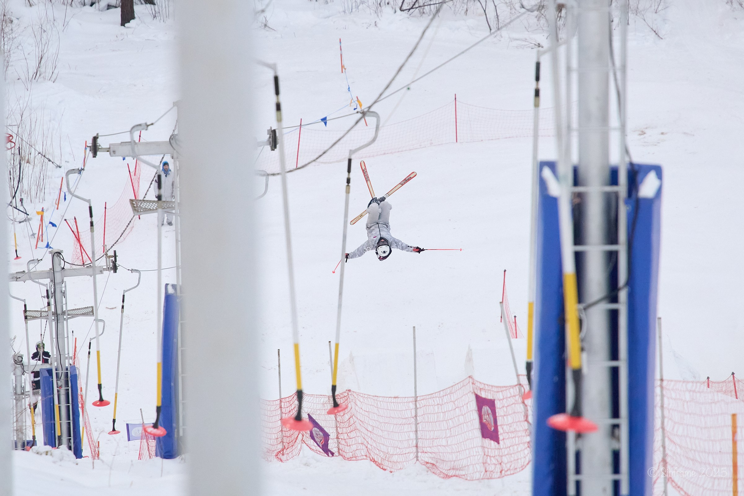 Тренировочный прыжок спортсмена по фристайлу, вид сквозь подъёмник.