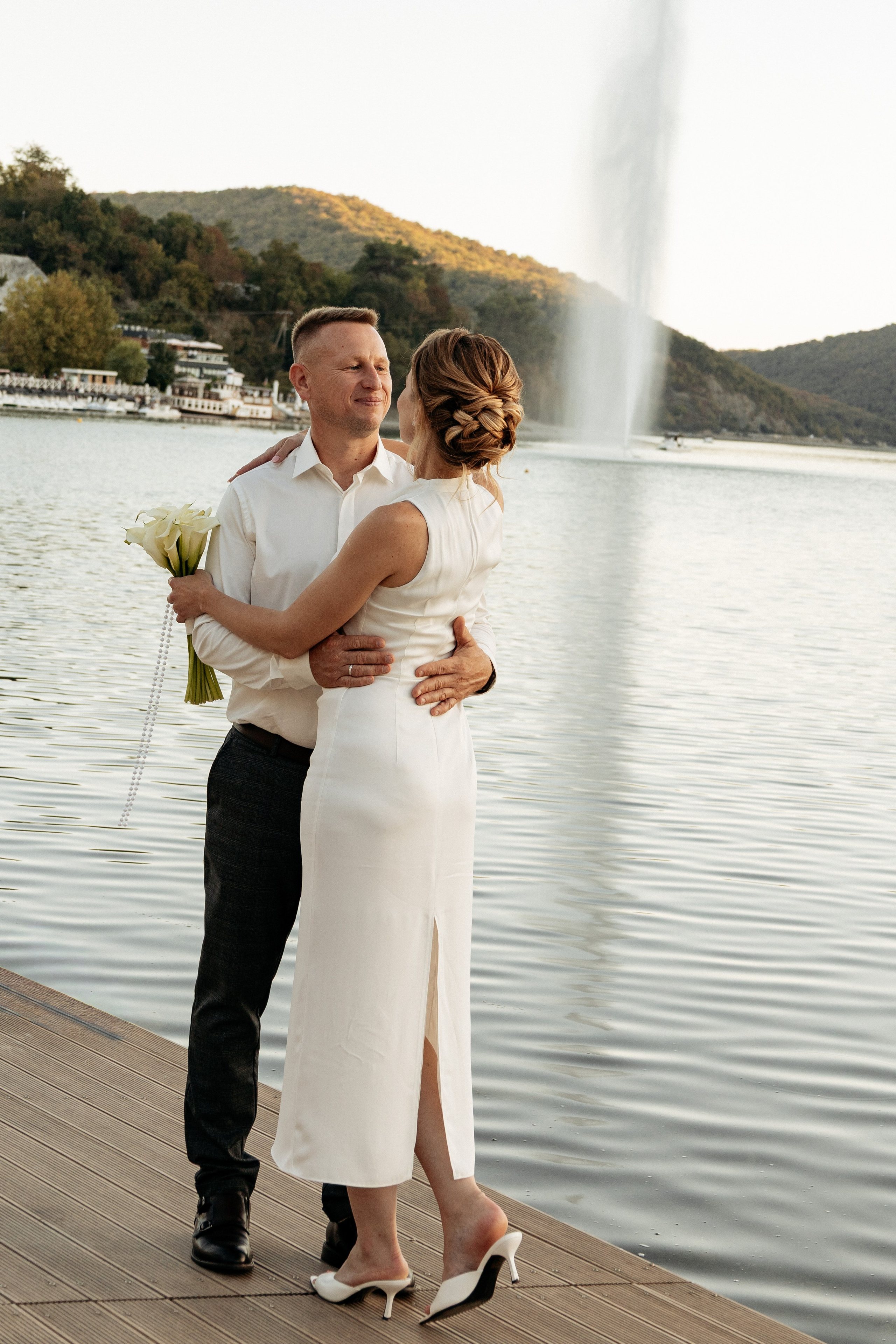 Невеста и жених обнимаются на зеленом склоне холма