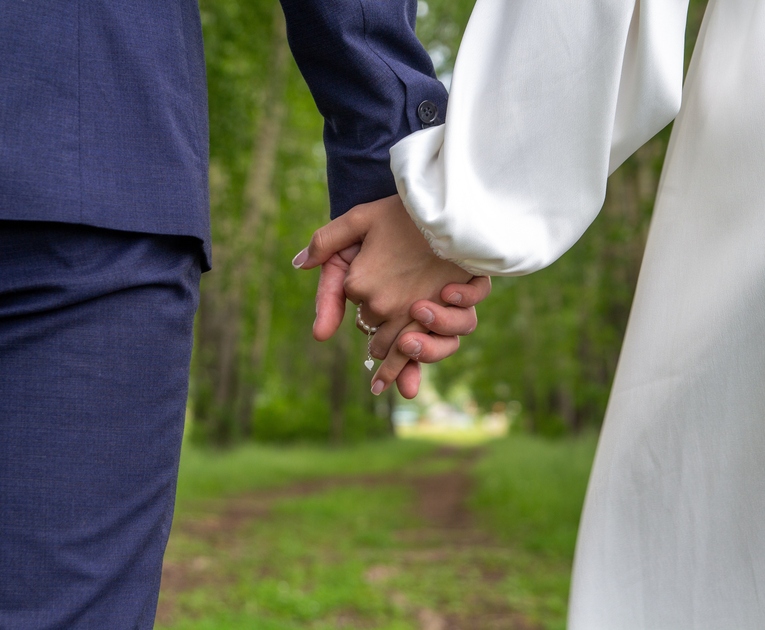  Крупный план — жених и невеста держатся за руки, идут по лесной тропинке.