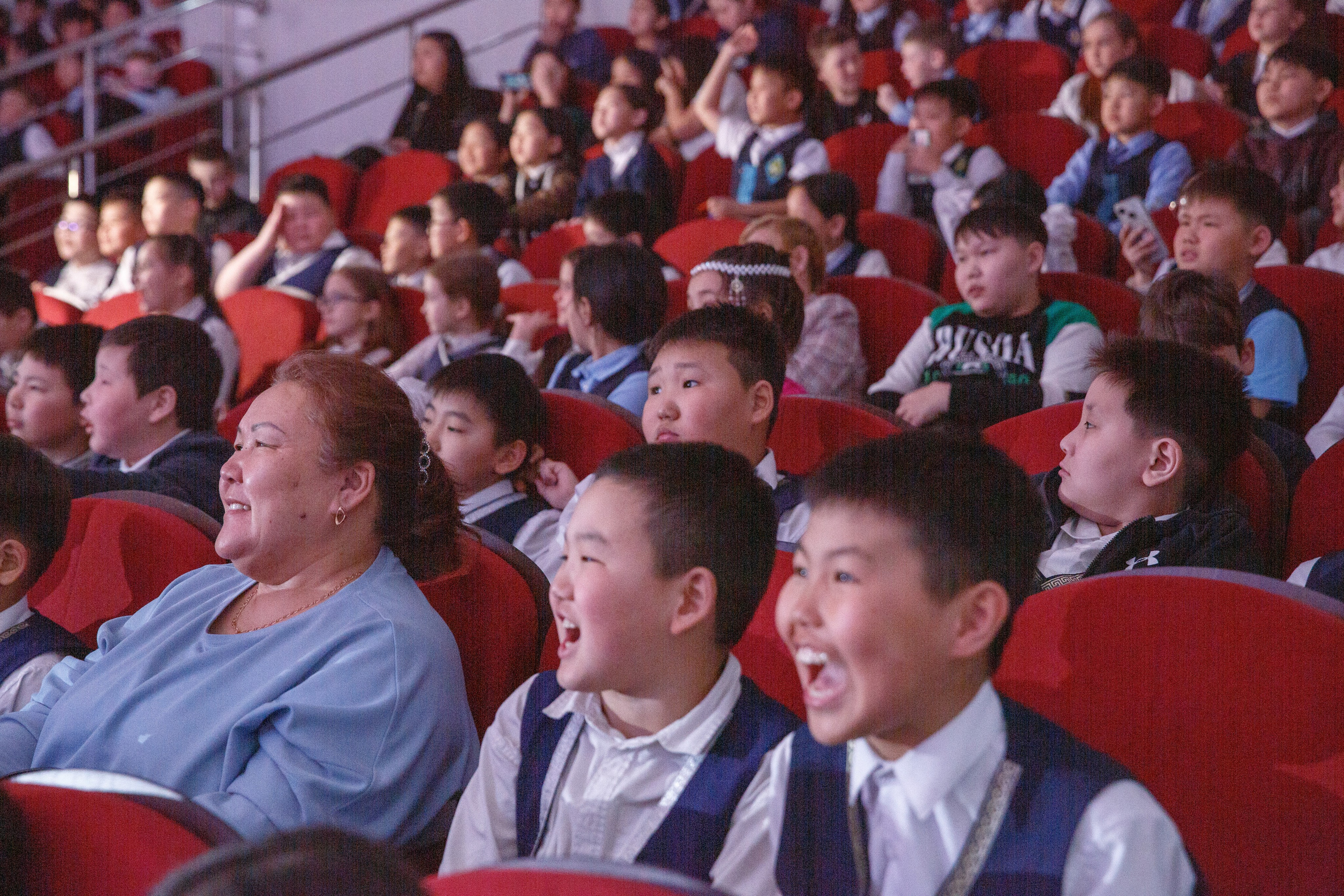 Дети и взрослые сидят в зале, наблюдая за выступлением.