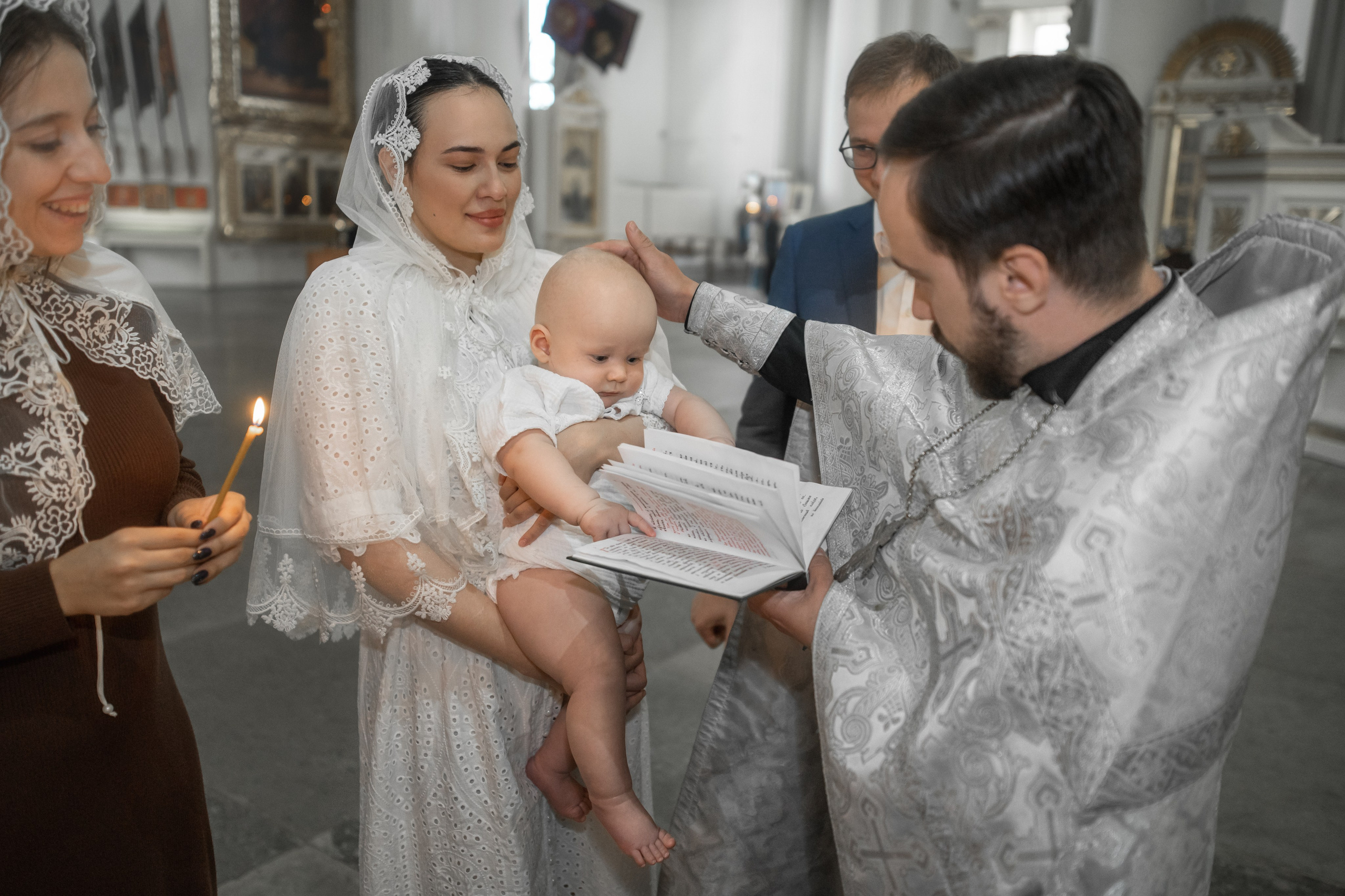 Малыш листает книгу в руках у батюшки