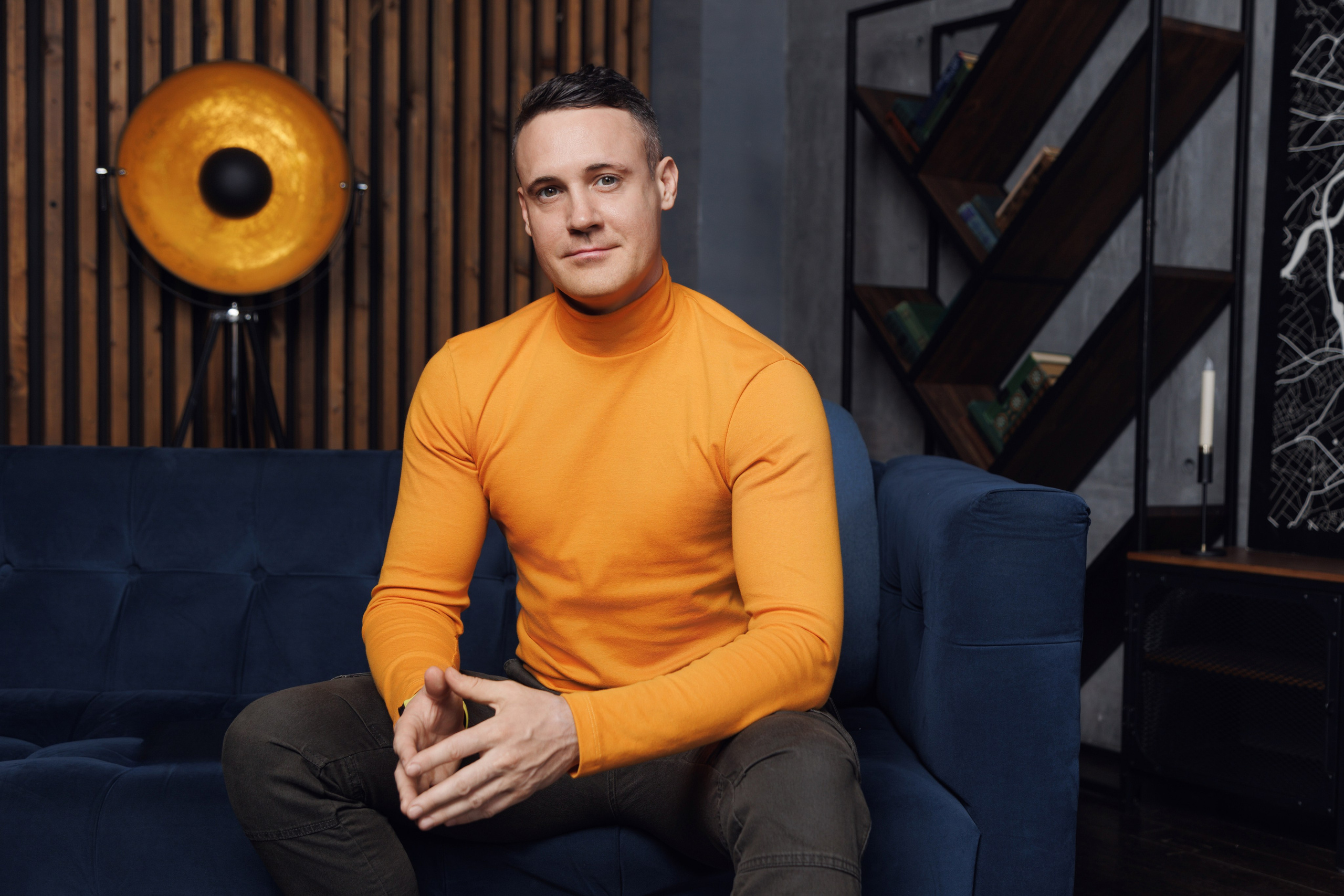 Мужчина в деловом стиле сидит на фоне современного офисного интерьера.