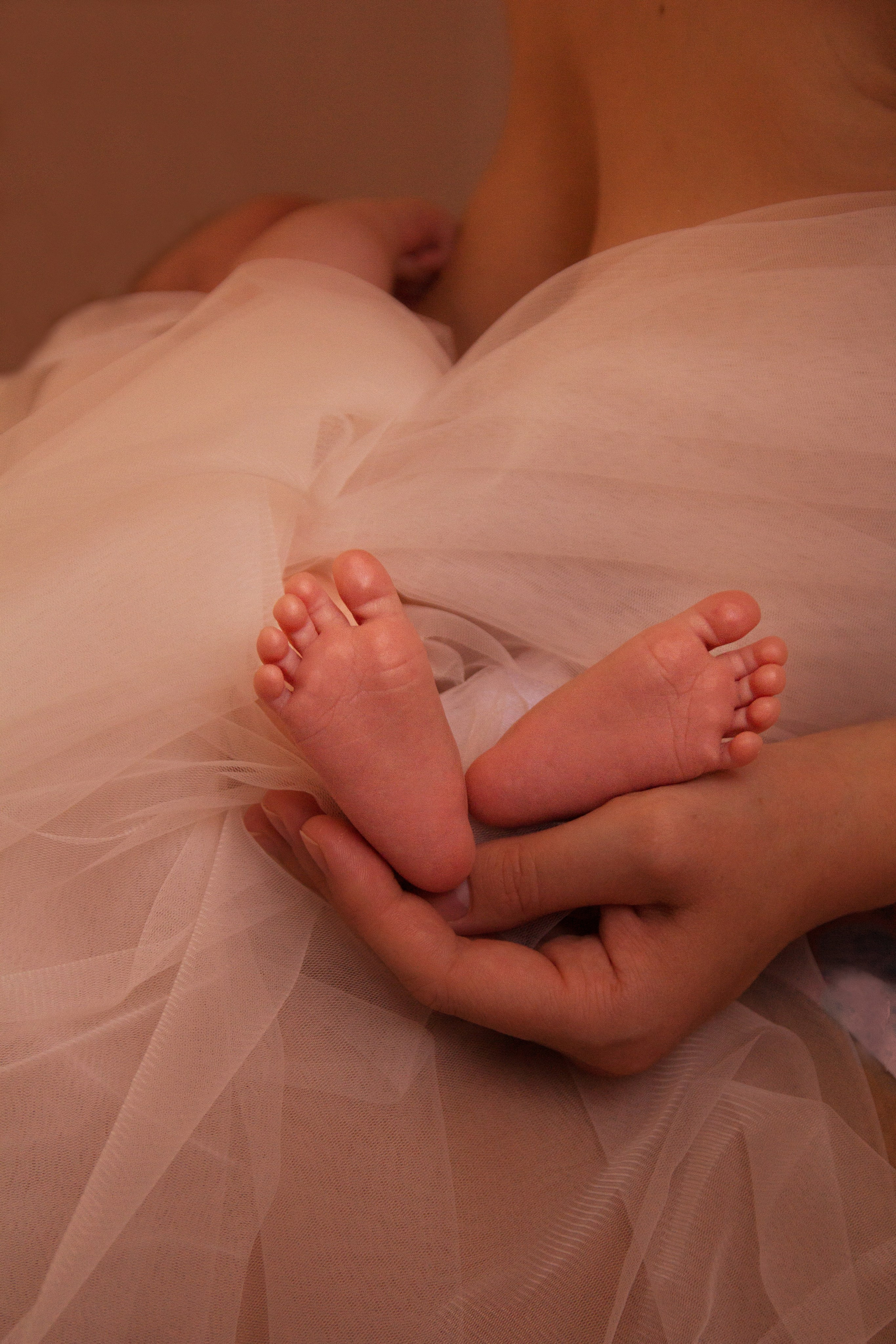 Женщина держит   в своей руке ножки младенца, закутанные в белый шифон.