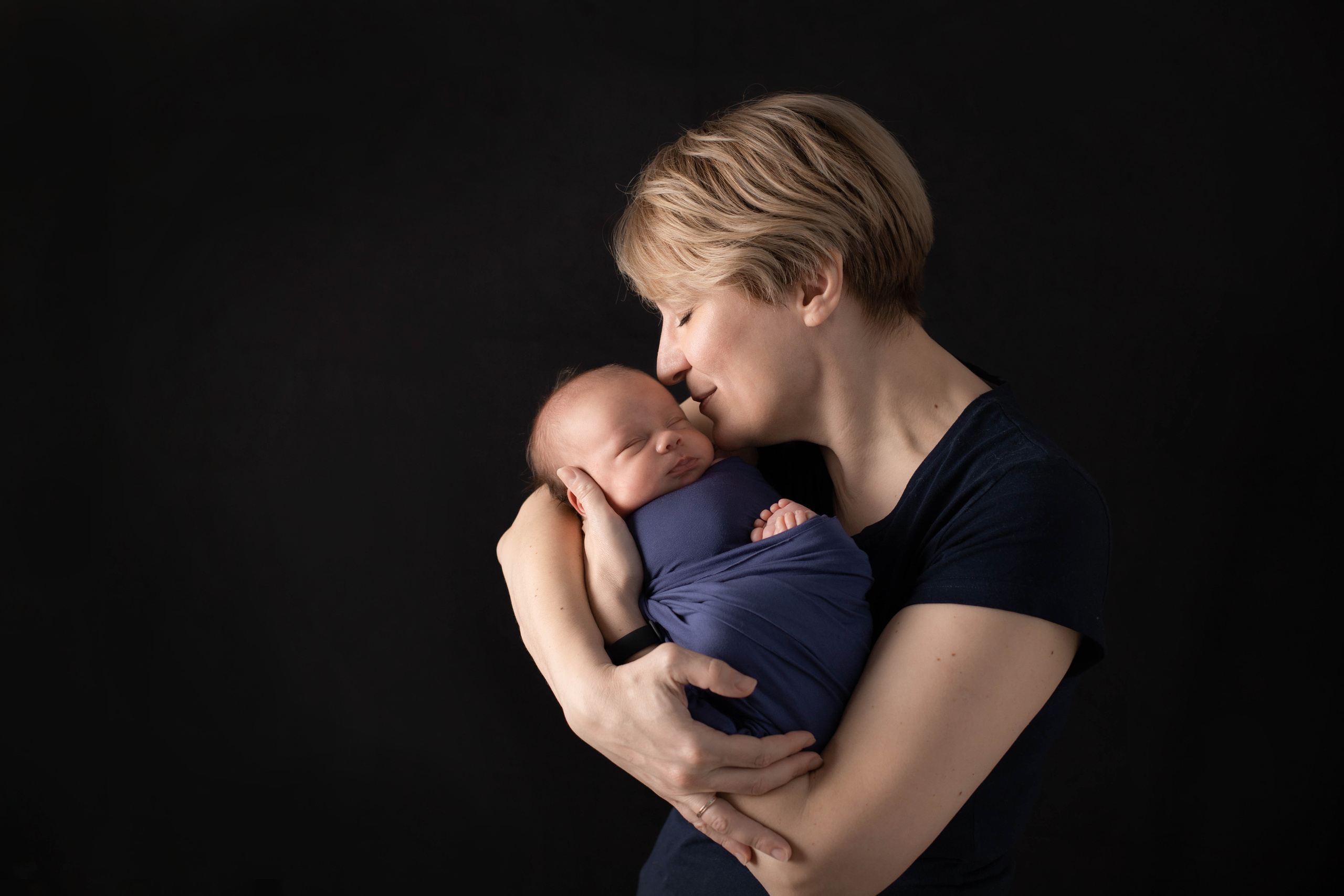 Фотография мамы нежно целующей новорожденного сына во время фотосессии ньюборн