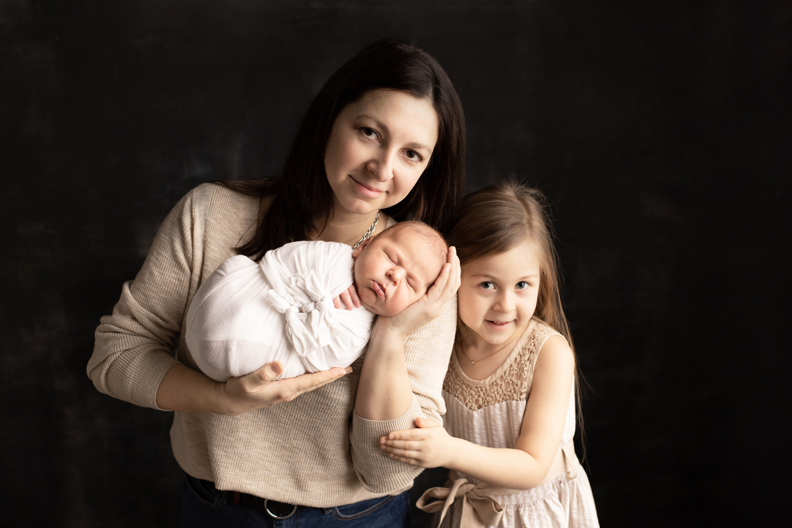 Фотография мамы, дочки и новорожденного малыша в студии на темном фоне