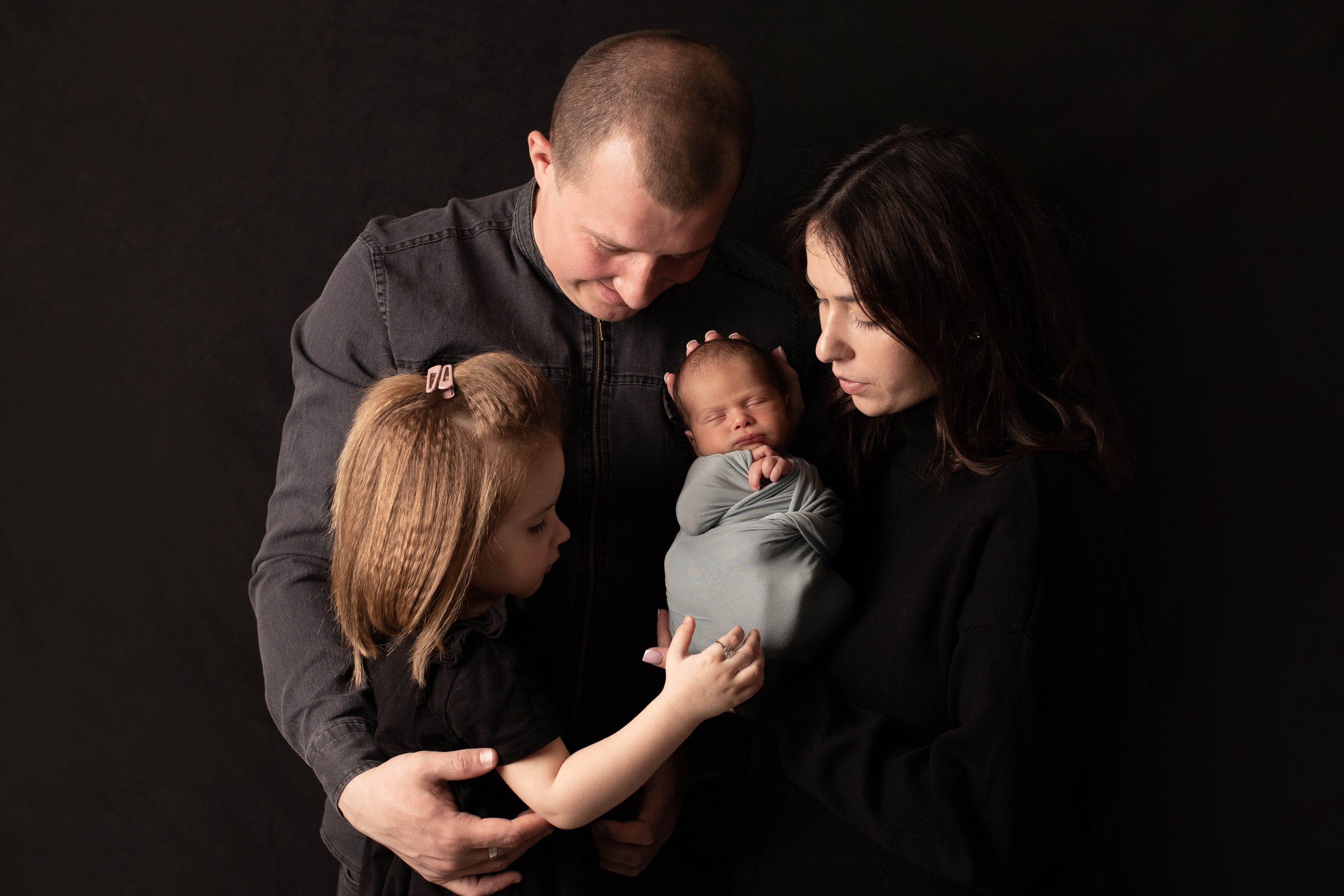 Фотография семьи со старшей дочкой  и новорожденным малышом. Все с большим интересом и любопытством смотрят на новорожденного мальчика. 