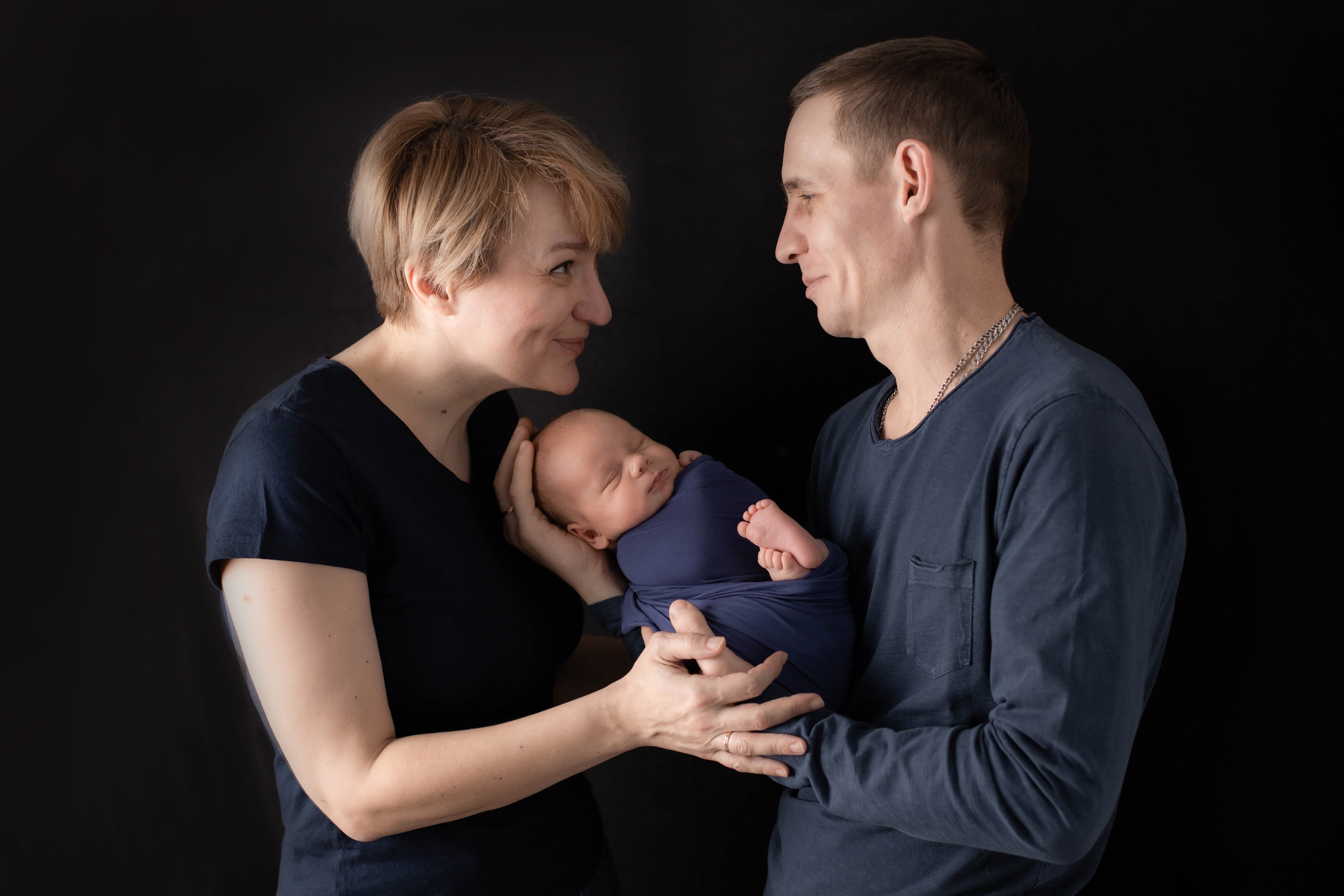 Фотография счастливых родителей со своим крошечным новорожденным сыном. Родители счастливо и с любовью смотрят друг на друга