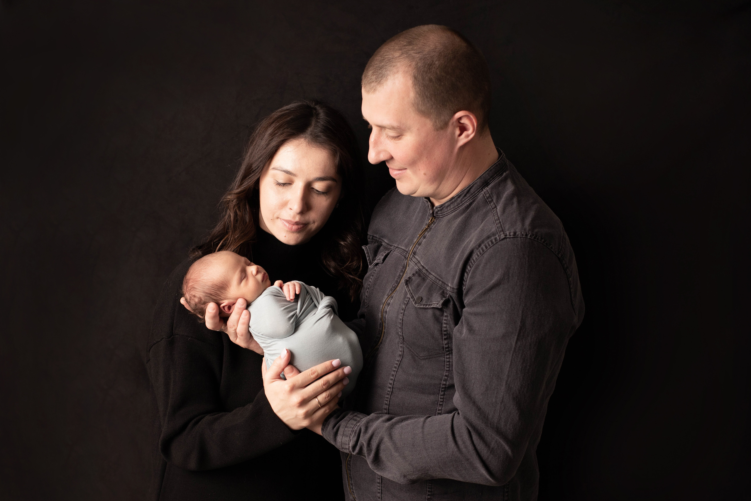 Фотография родителей с новорожденным малышом на руках на темном фоне. 
