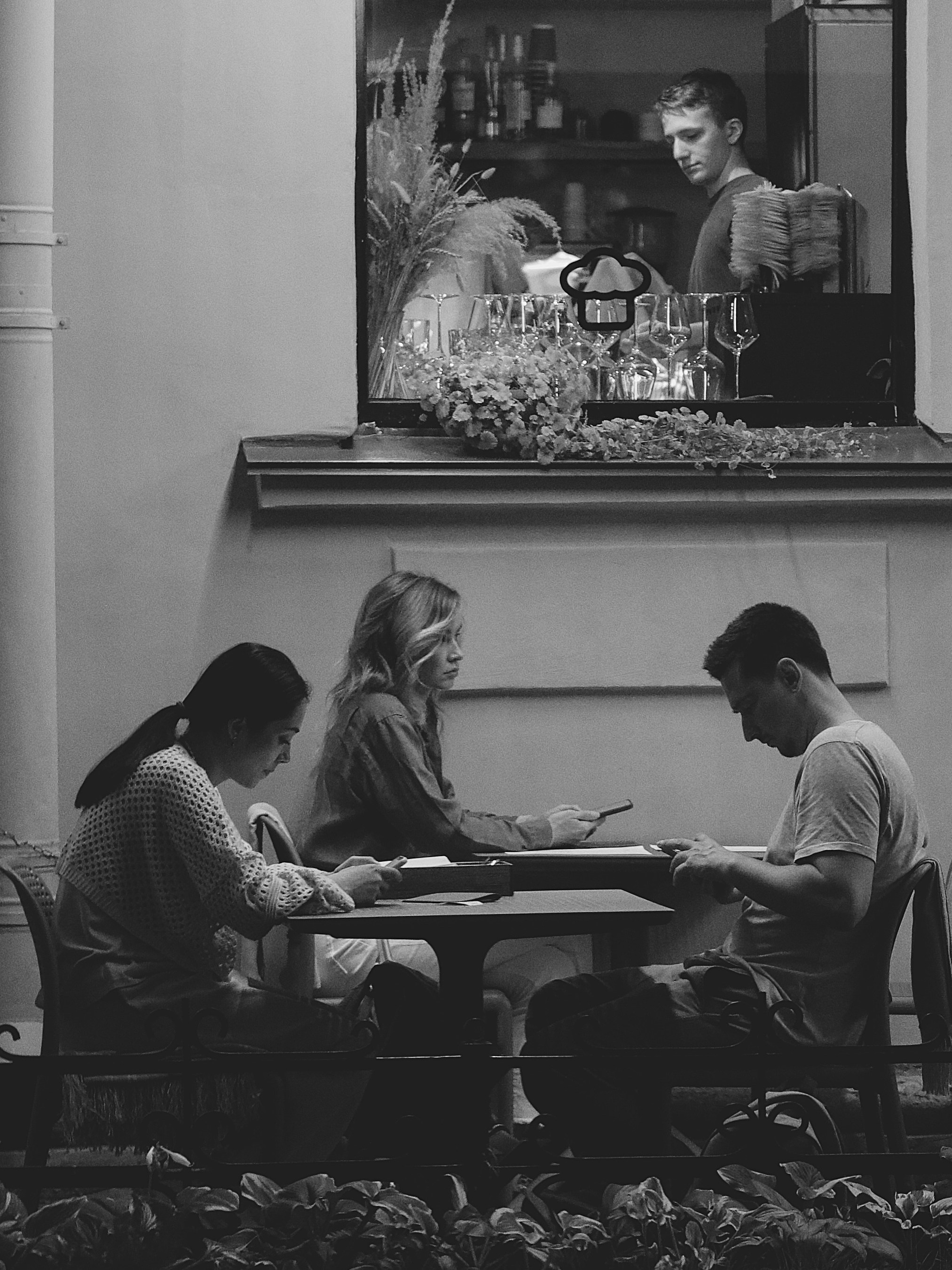 трое людей сидят под окном, четвертый смотрит на них из окна