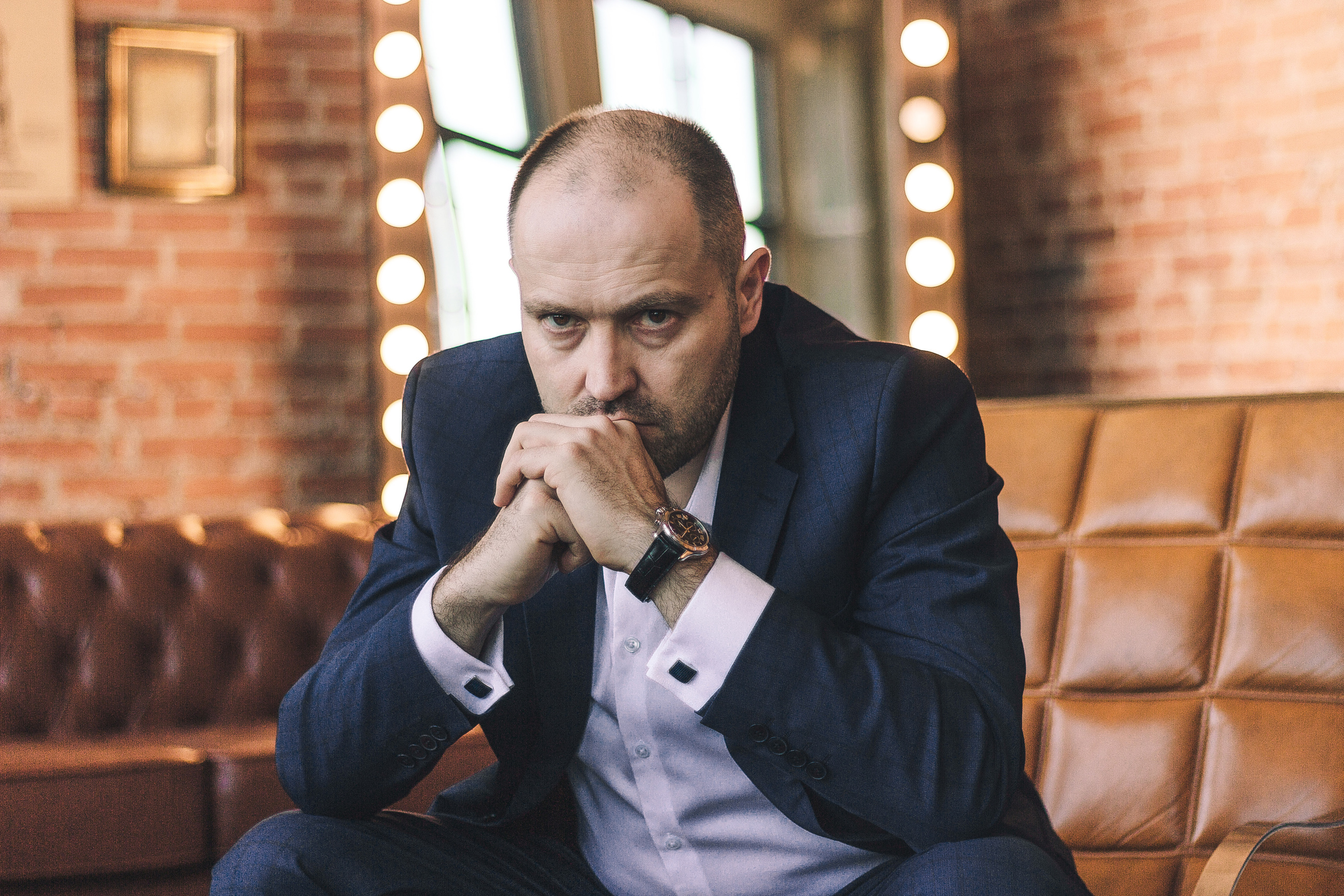 Мужчина в деловом костюме с серьёзным взглядом сидит в кресле