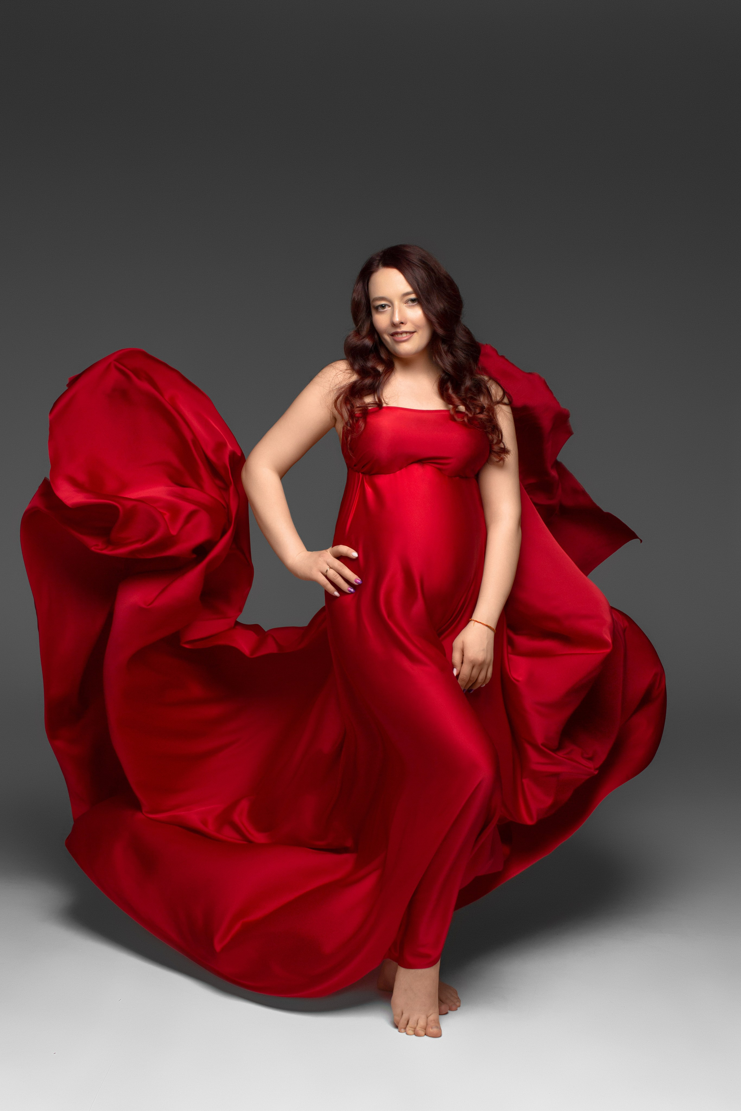 беременная девушка в шелковой красной ткани, которая развивается за спиной 