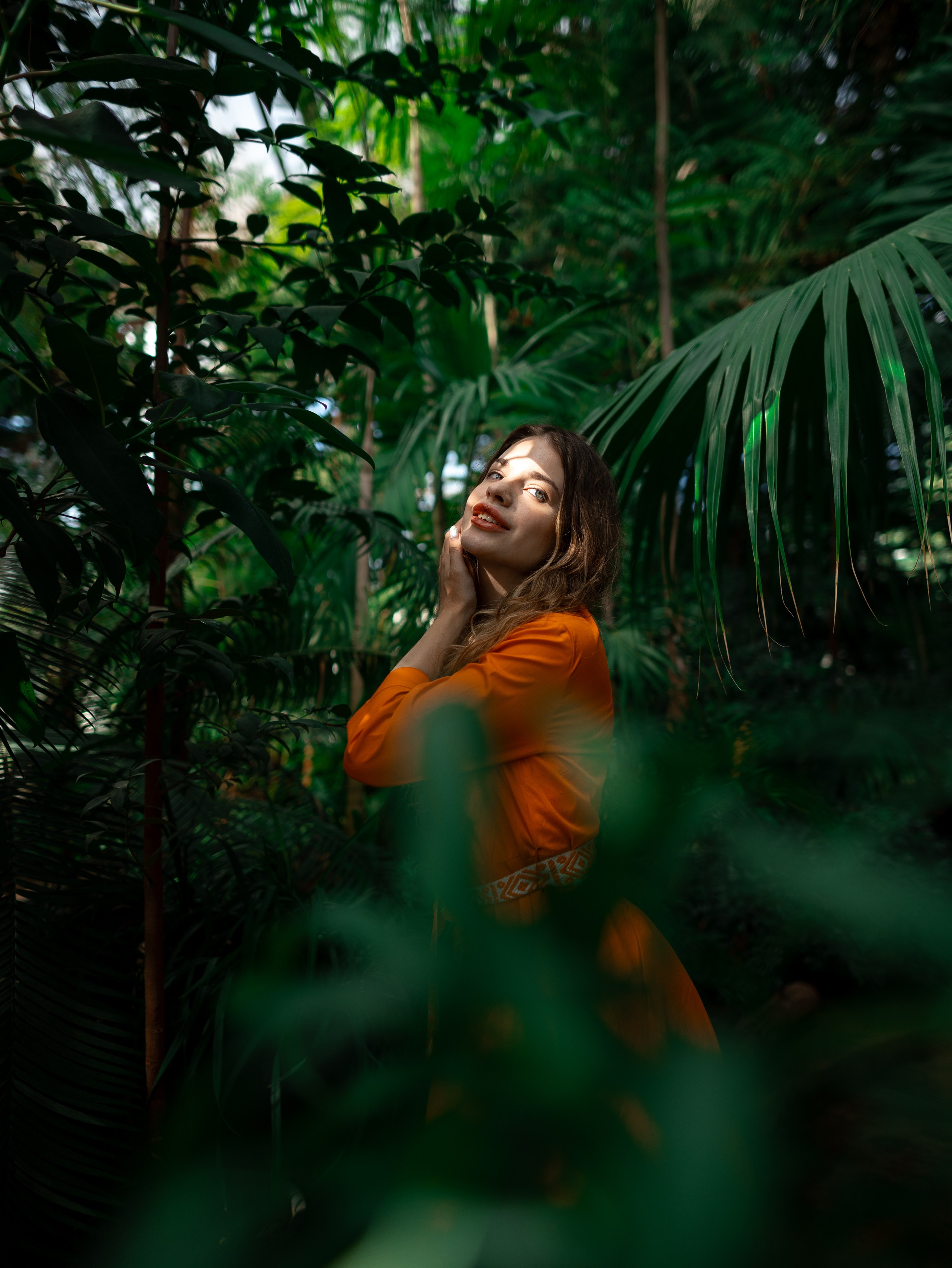 Девушка в оранжевом платье стоит на фоне зелени