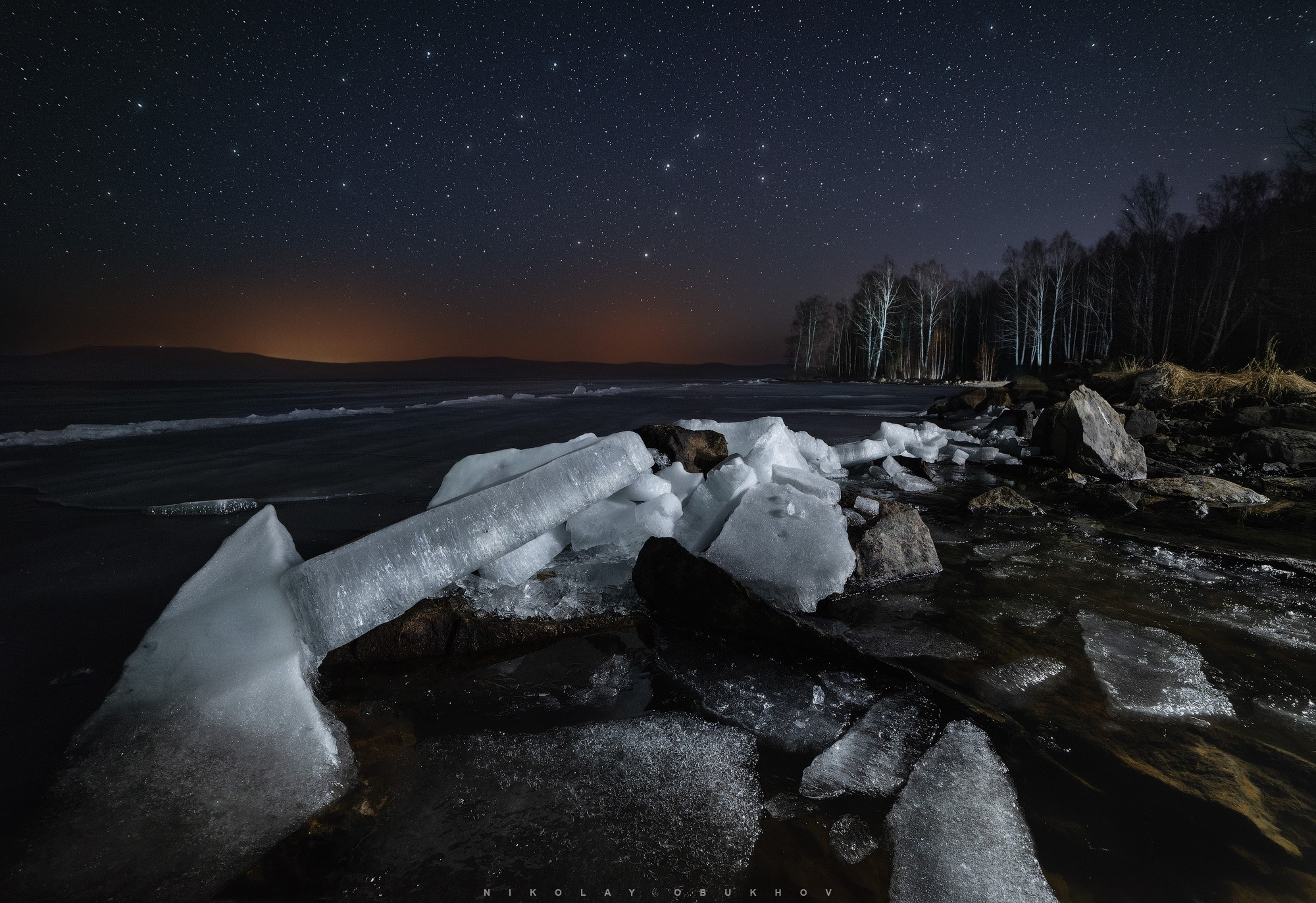 Под звёздным куполом — ночной весенний пейзаж с ночным звездным небом, каменистым берегом и тающими льдинами.