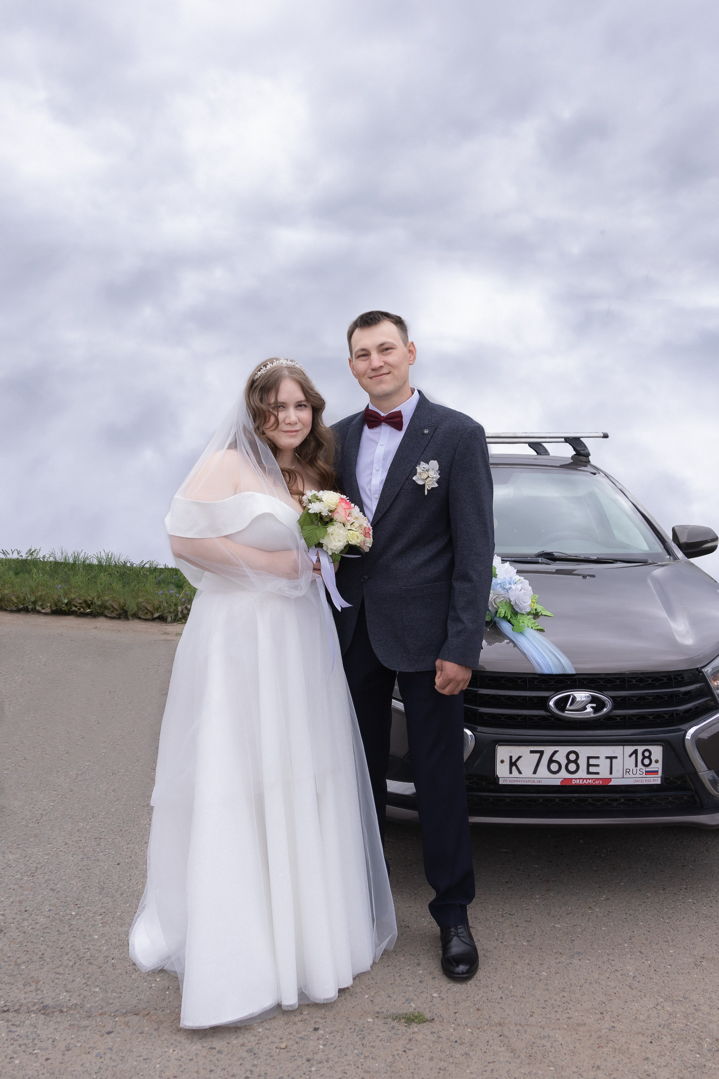 Невеста с женихом стоят возле машины украшенной цветами