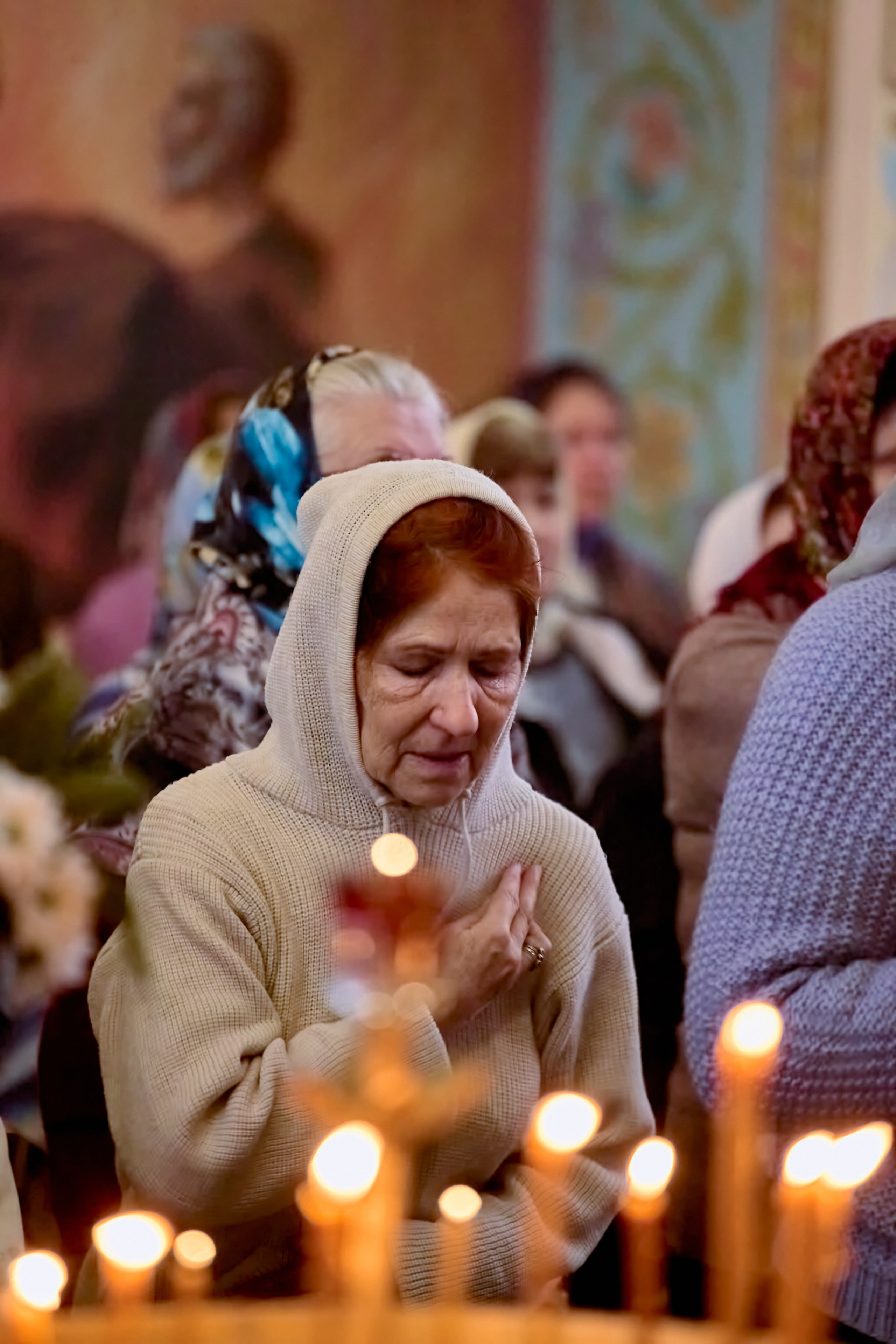 Подсвечник со свечами перед ним стоит женщина и молится