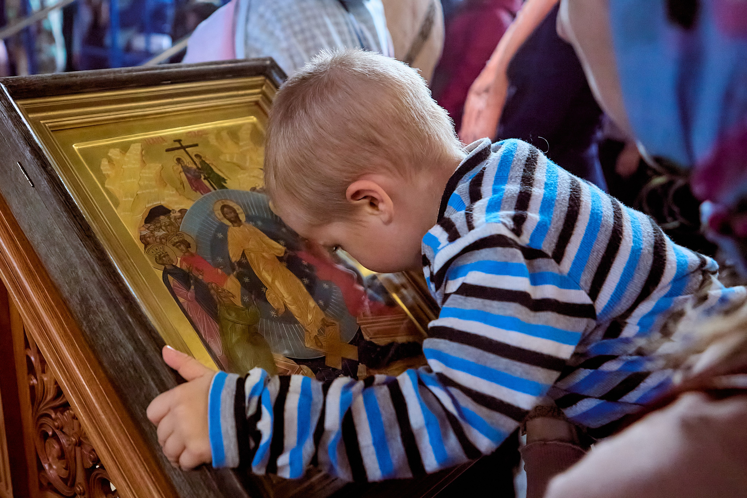 Мальчик на руках у мамы приклонил голову перед иконой и целует саму икону