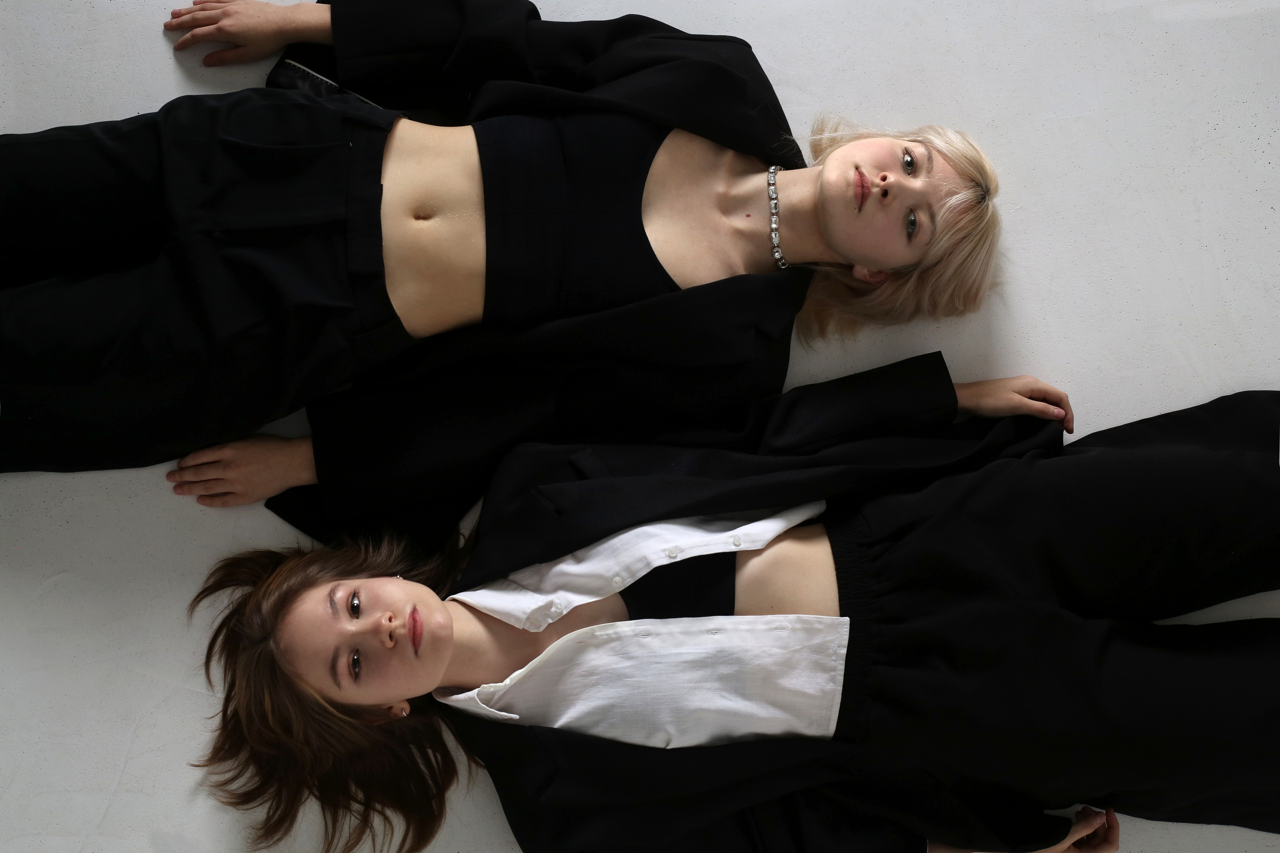 Минималистичная фотосессия: две девушки в черных костюмах лежат на полу в студии
