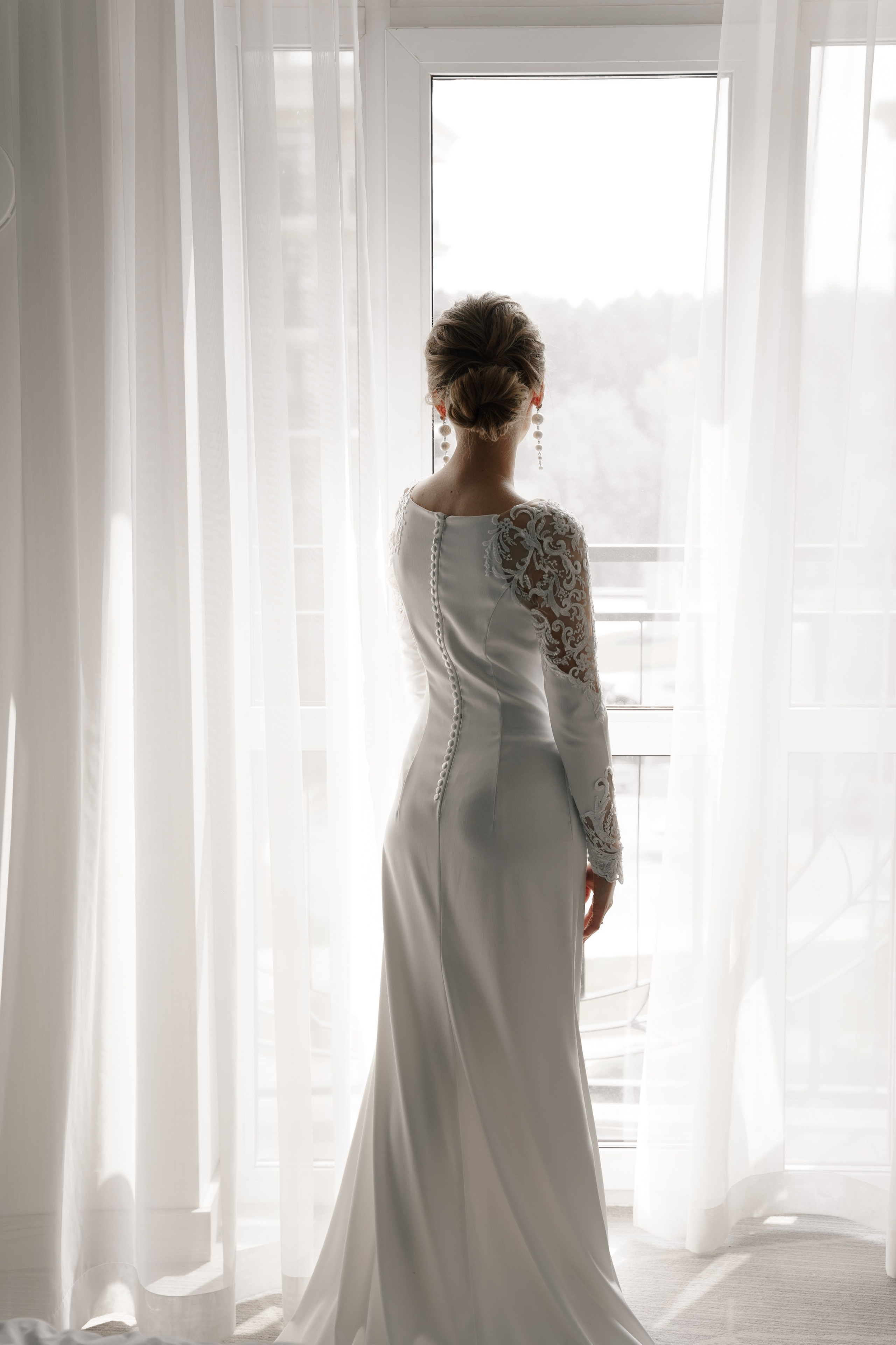 Невеста у окна в гостинице фото со спины