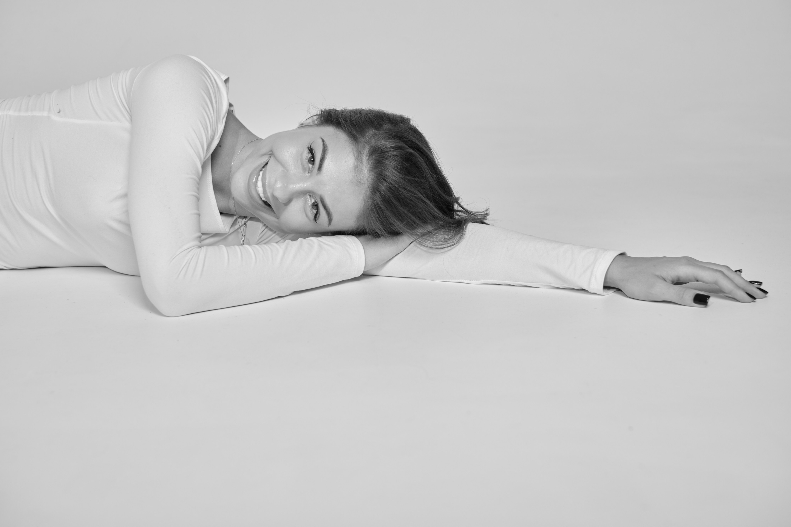 Черно-белая фотография: девушка-модель лежит на полу, закинув ноги на белый куб. Креативное позирование для тестов.
