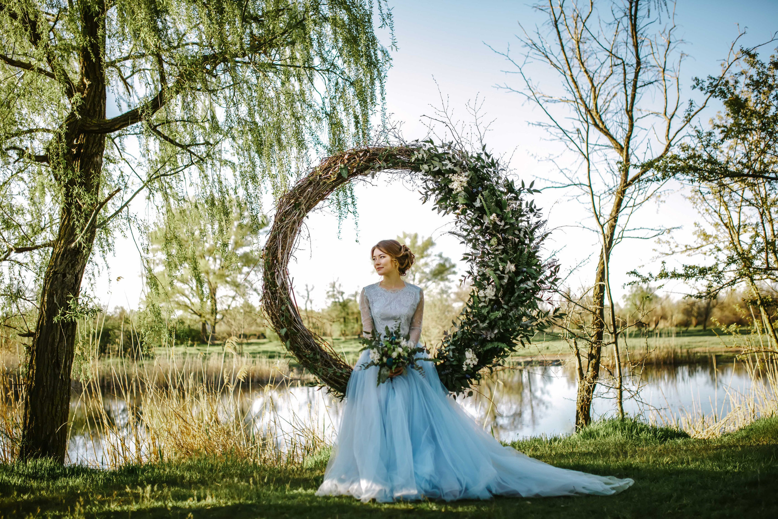 Невеста в голубом свадебном платье сидит на свадебной арке