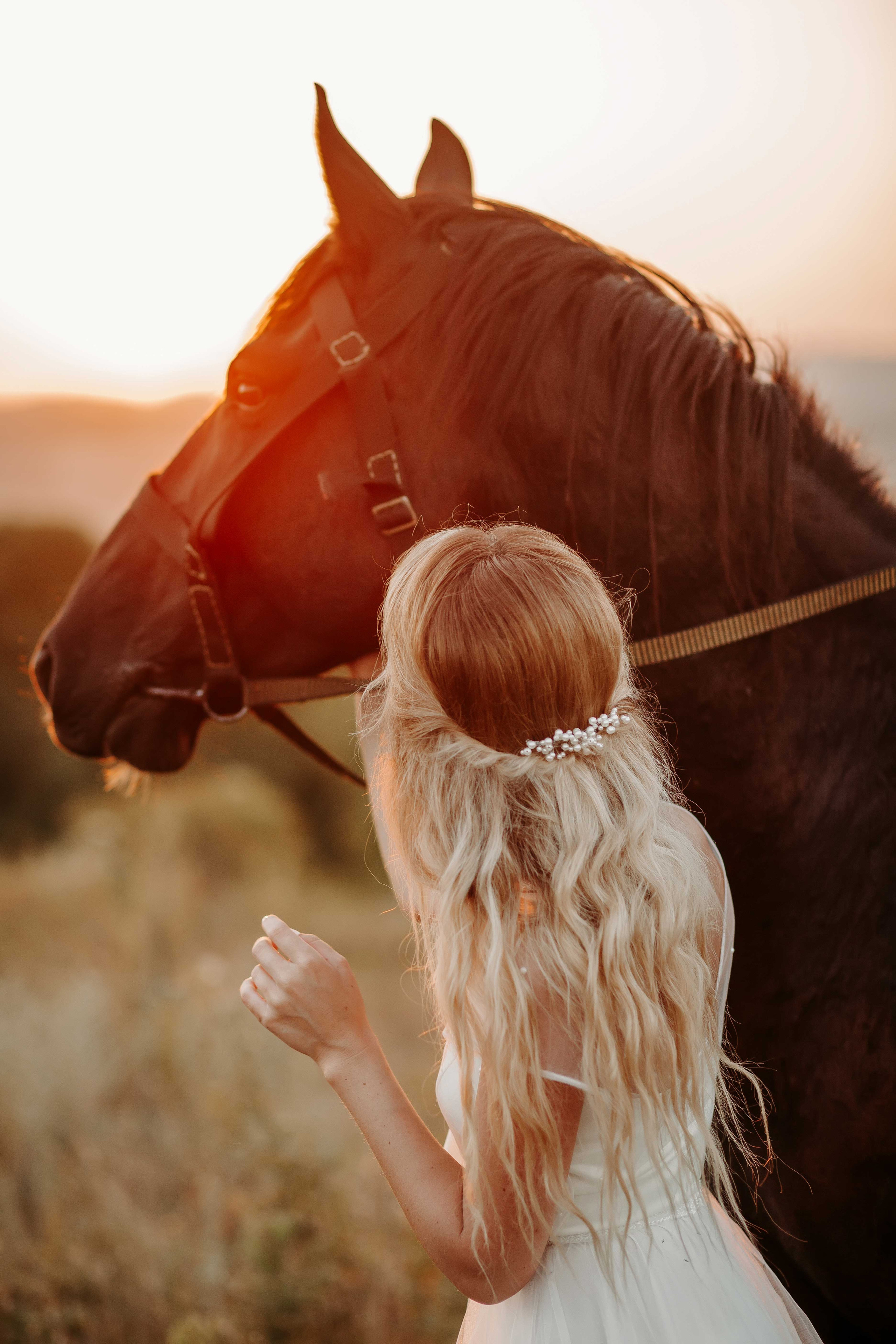 Блондинка невеста в белом платье стоит рядом с лошадью