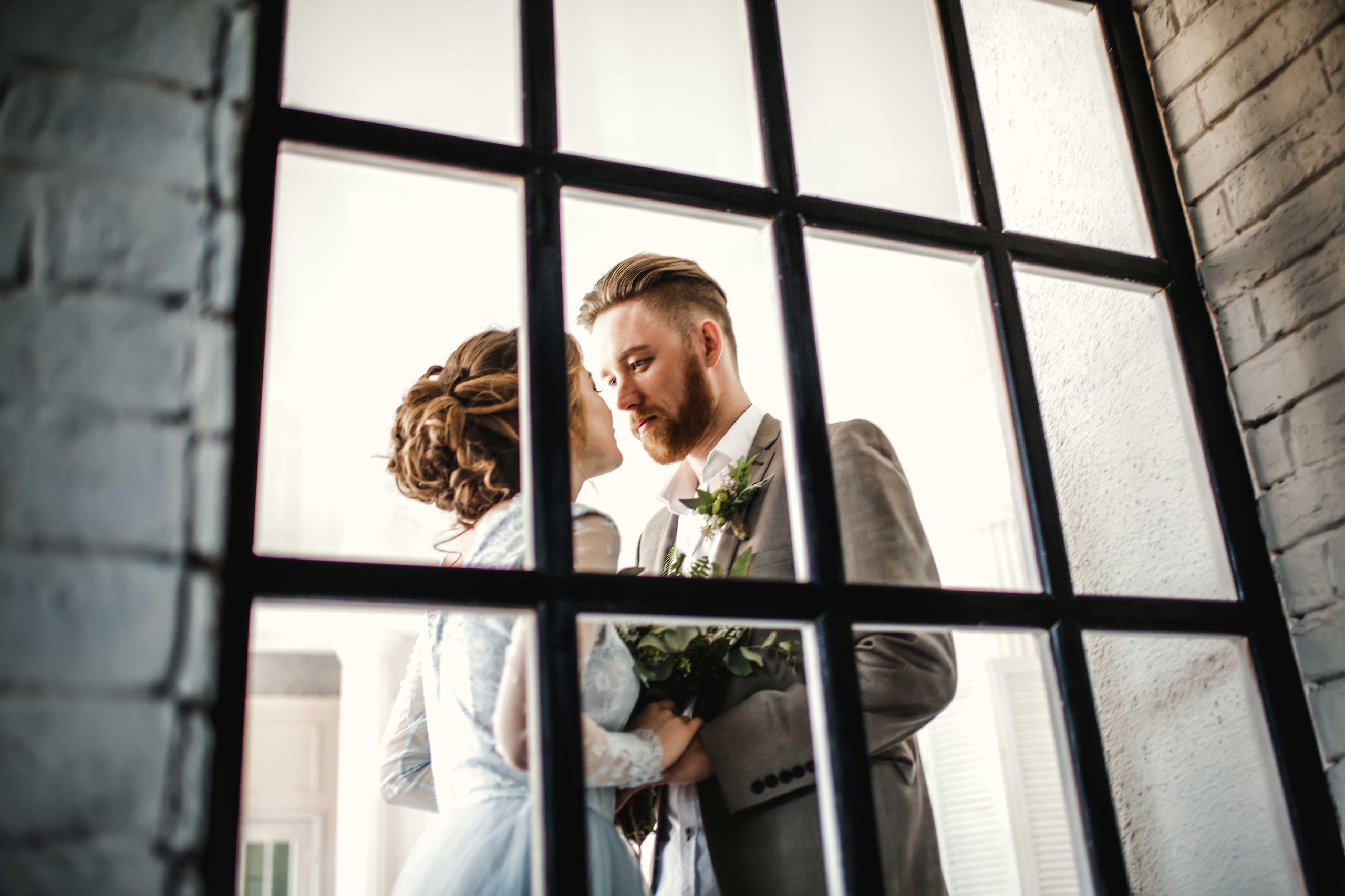 Нежная стильная невеста в голубом свадебном платье и высокий красивый жених с бородой стоят взявшись за руки