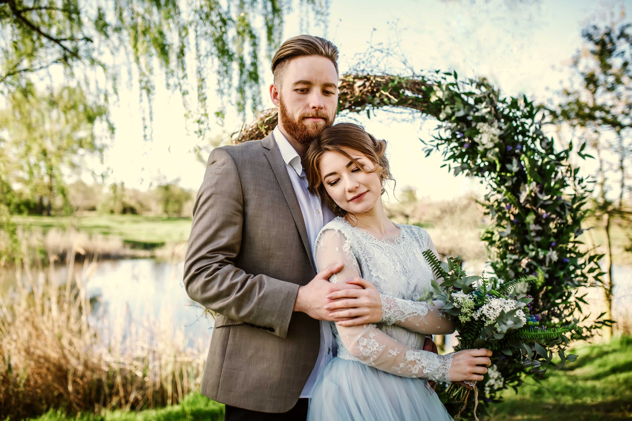 Нежная стильная невеста в голубом свадебном платье и высокий красивый жених с бородой стоят взявшись за руки