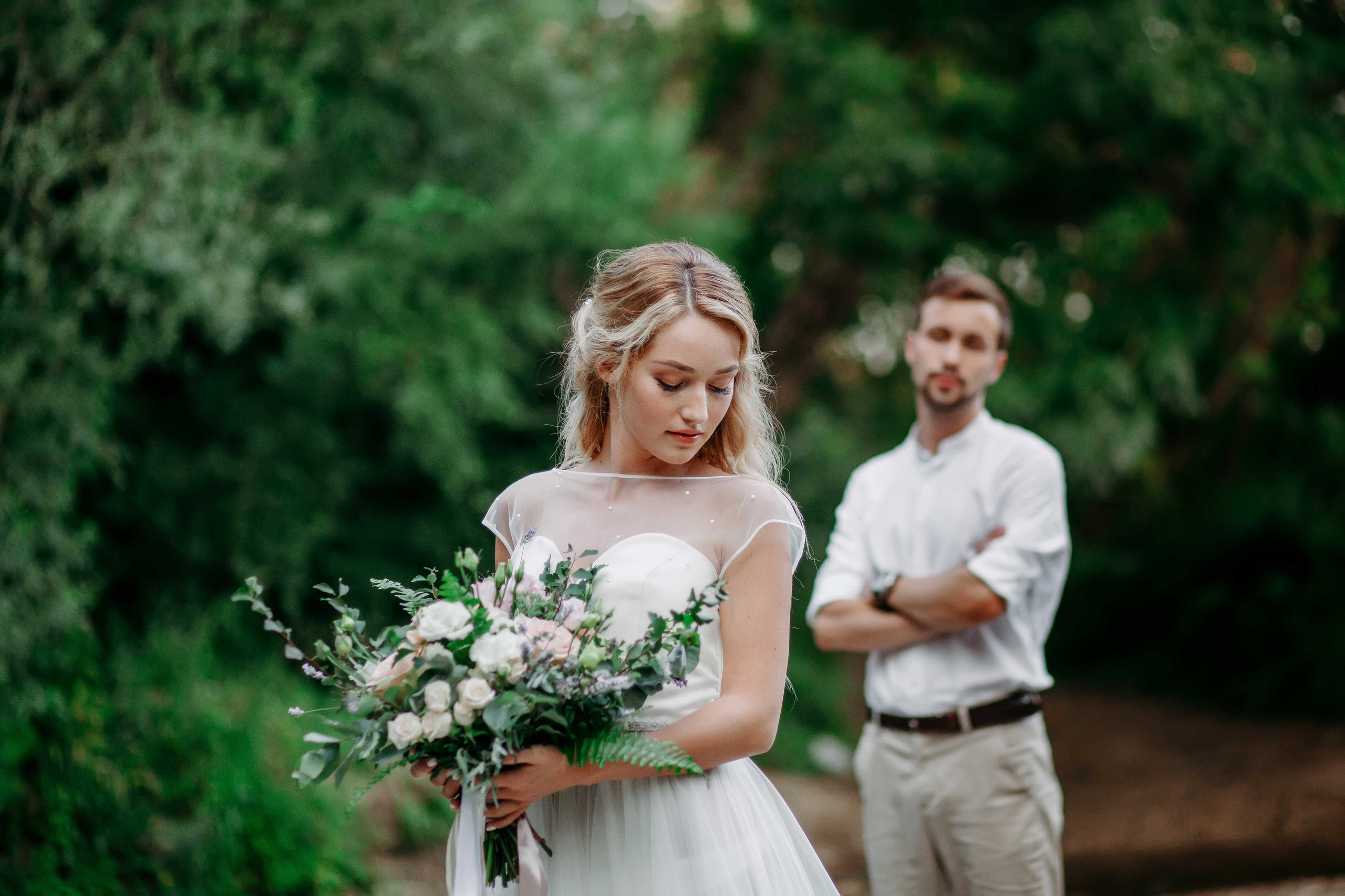 Невеста с распущенными светлыми волосами и жених в белой рубашке стоят на берегу реки 