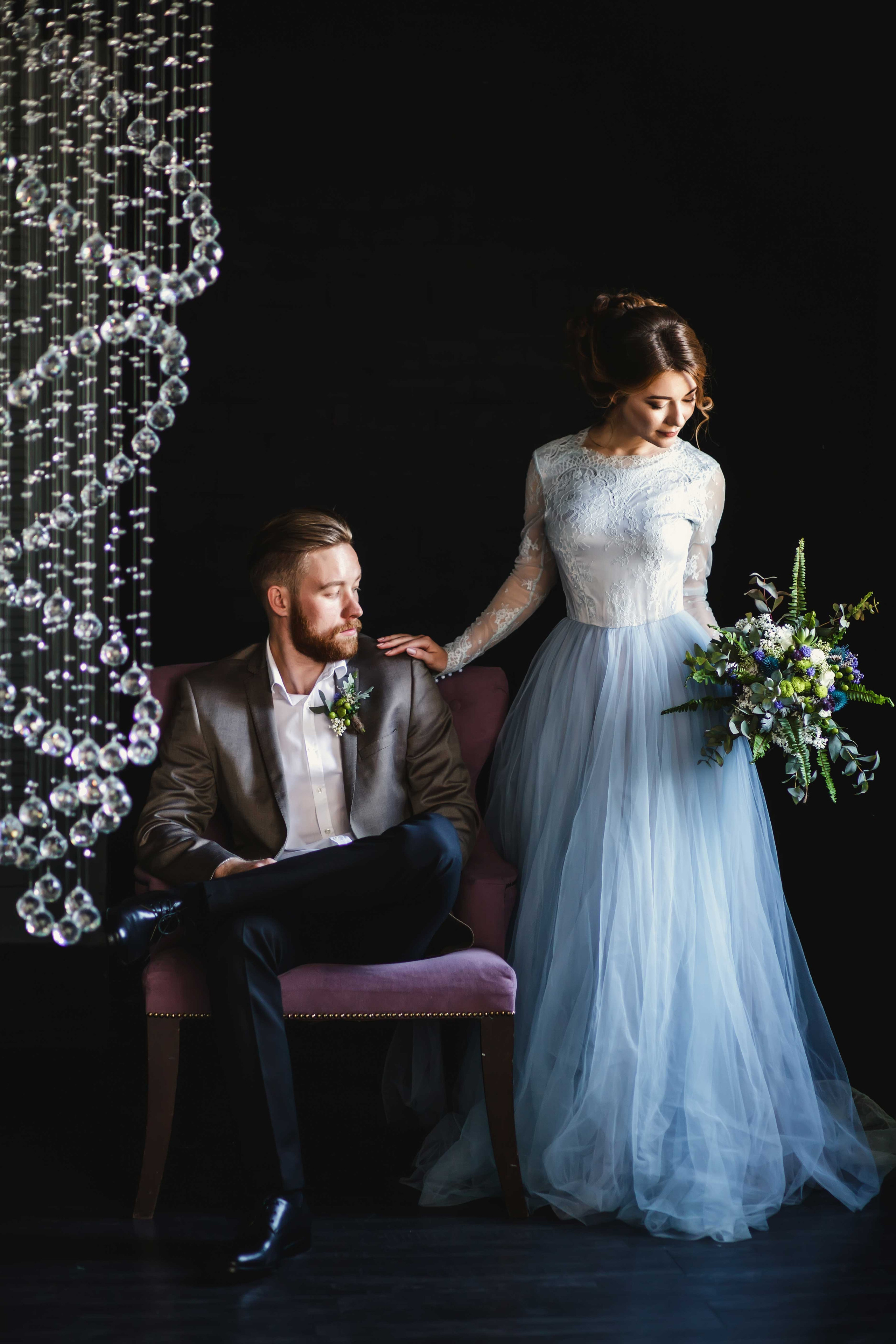 Нежная стильная невеста в голубом свадебном платье стоит рядом с женихом положив руку ему на плечо