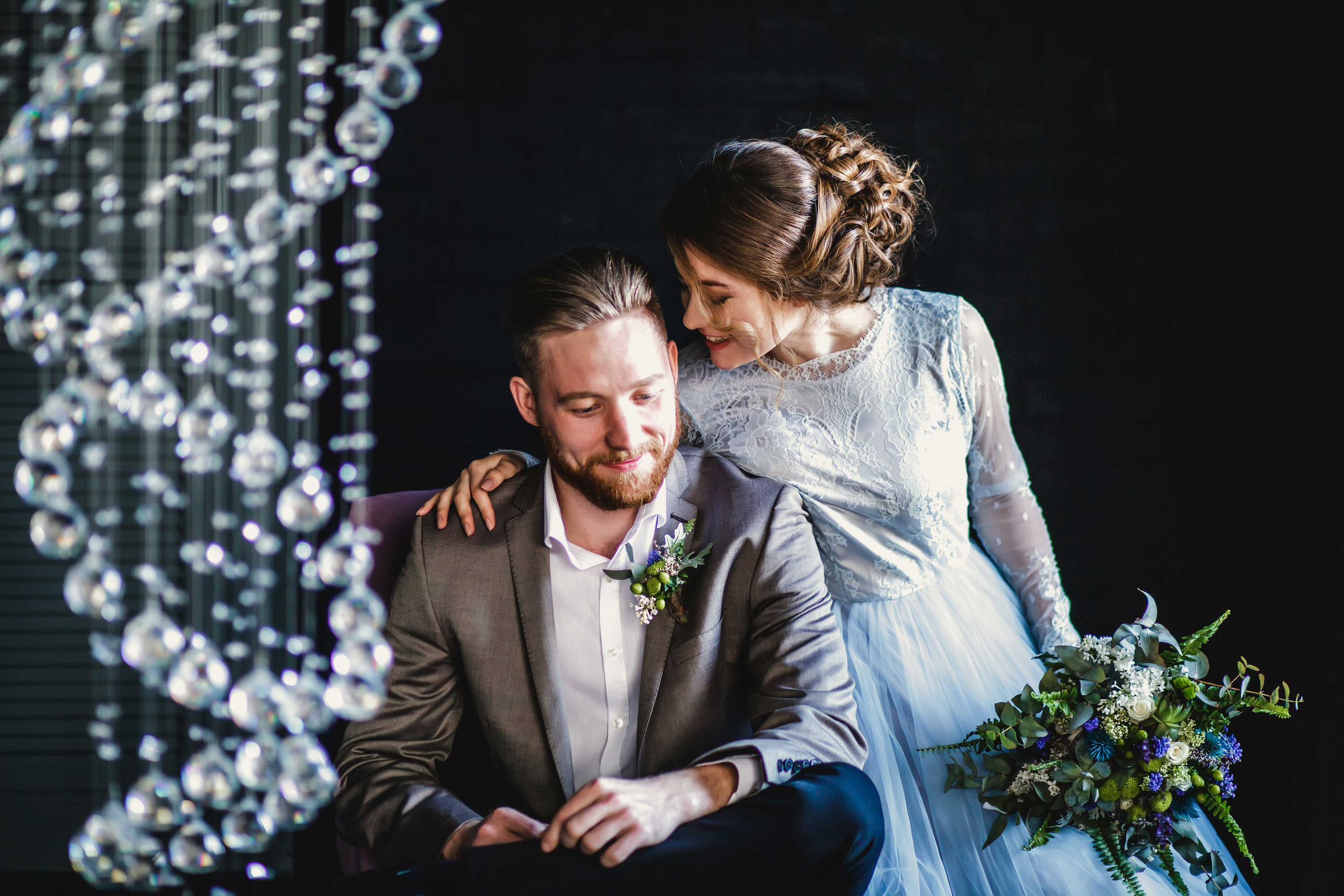 Нежная стильная невеста в голубом свадебном платье и высокий красивый жених с бородой сидят рядом 