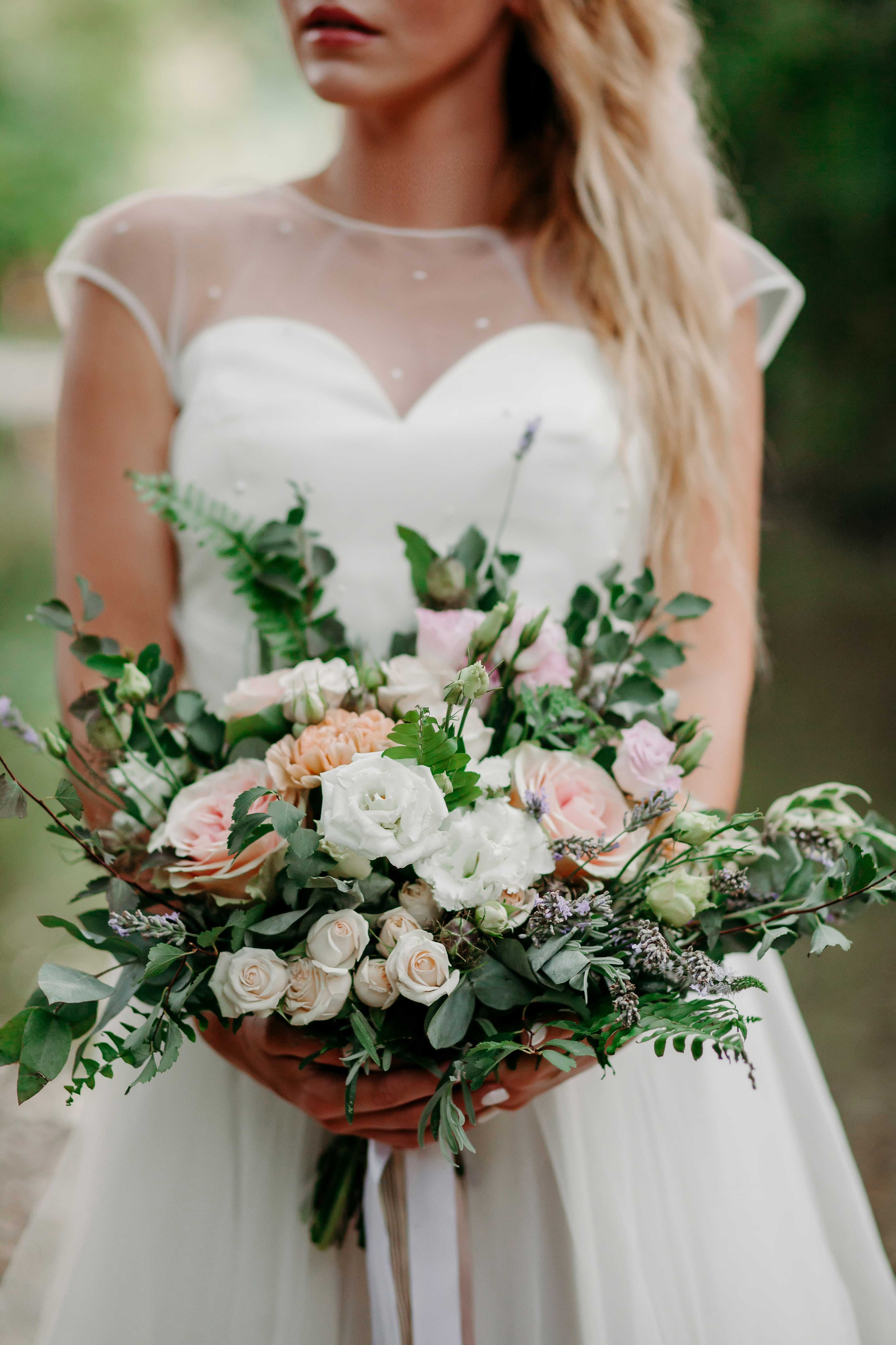 Невеста с распущенными светлыми волосами держит в руках свадебный букет