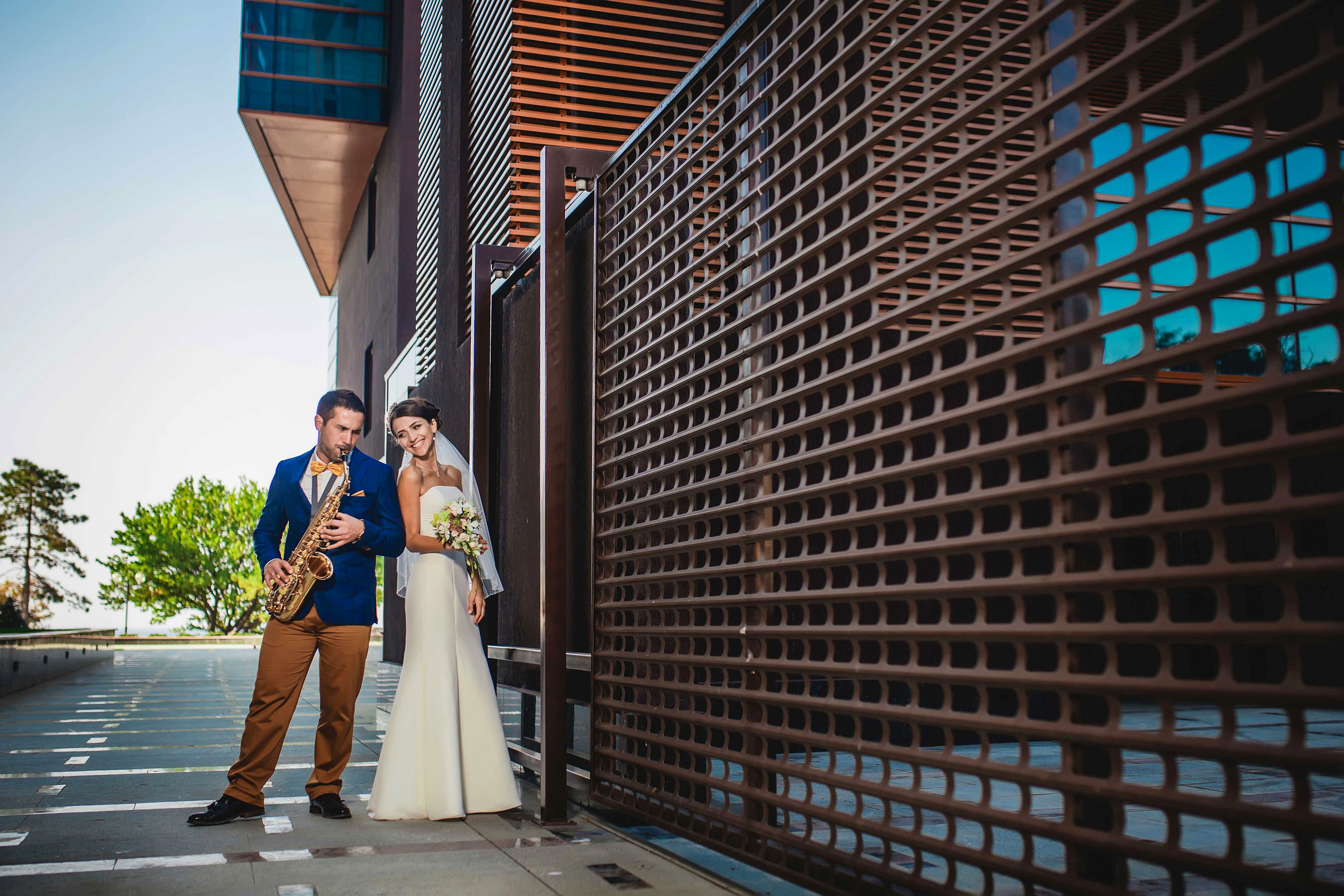 Жених играет на саксофоне а невеста  улыбаясь стоит рядом 