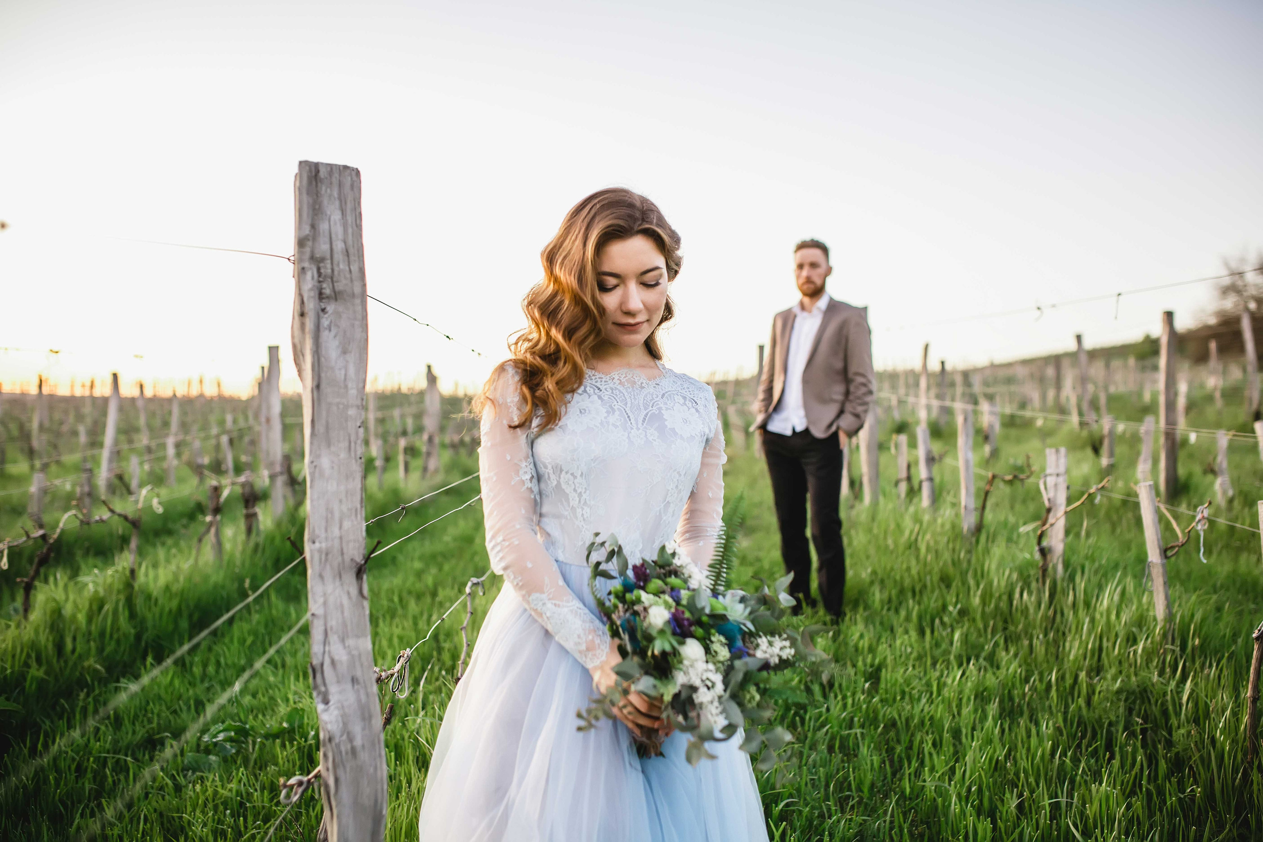 Нежная стильная невеста в голубом свадебном платье и высокий красивый жених с бородой  в виноградниках