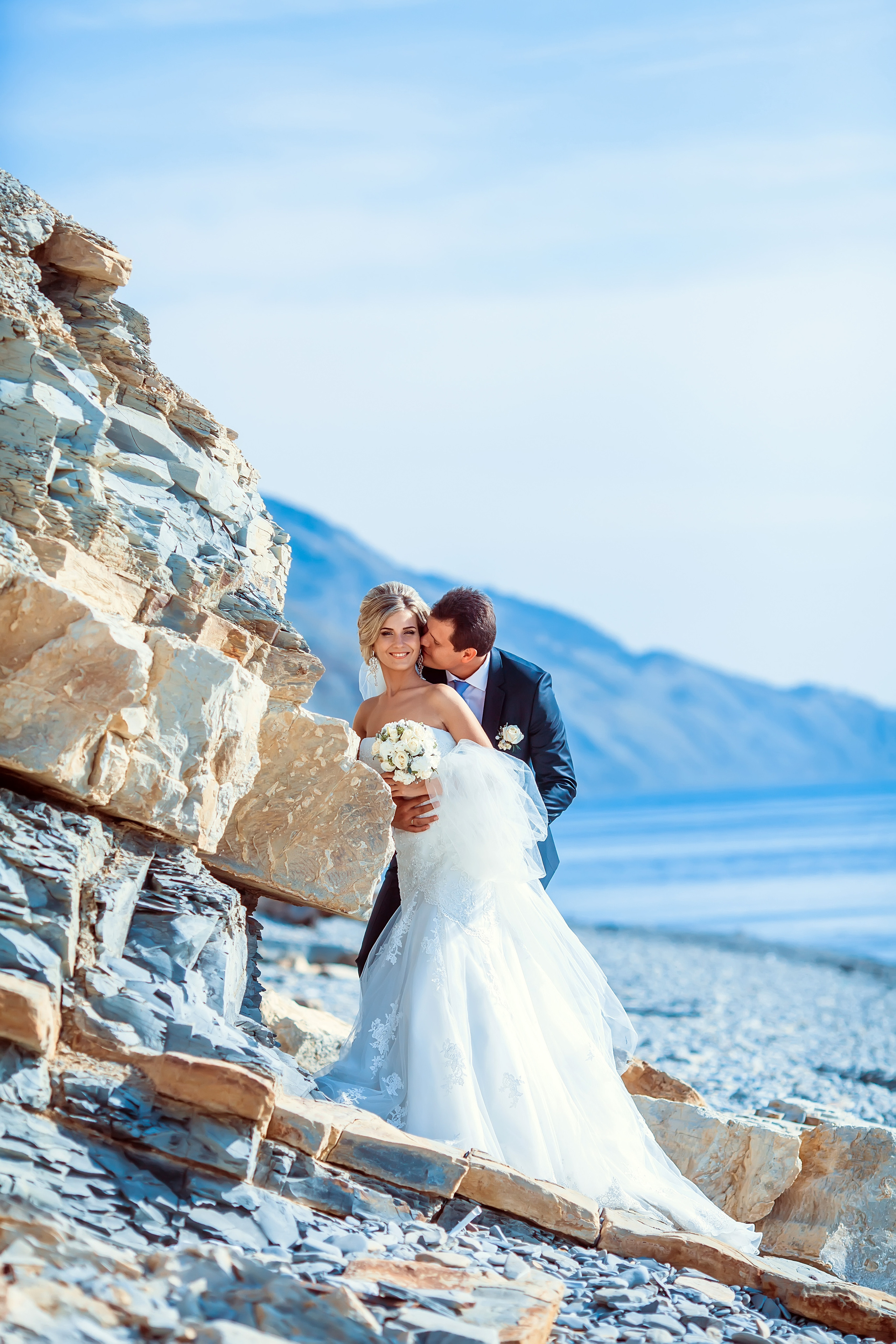 Жених и невеста стоят на фоне моря и скал обнявшись