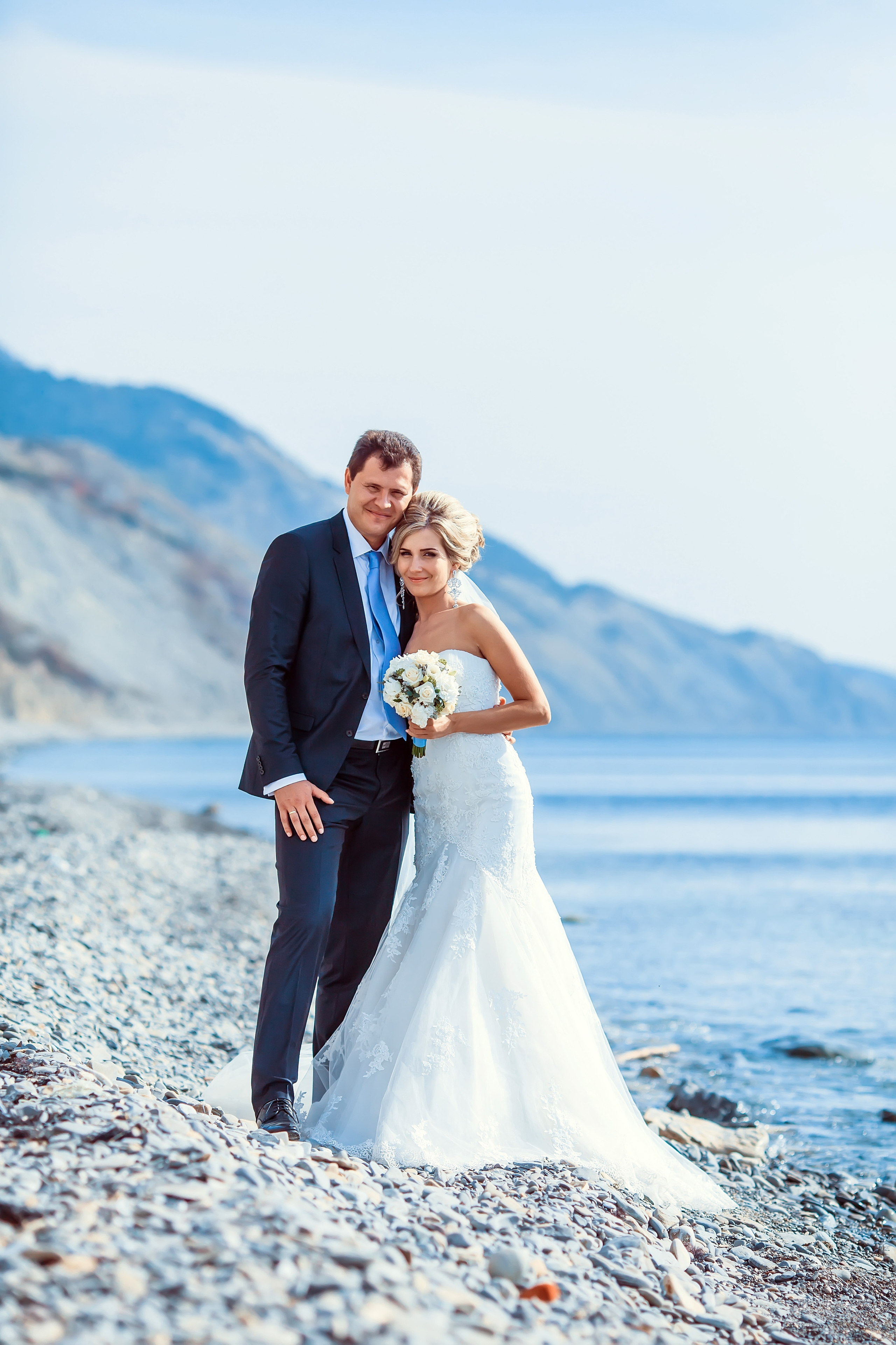 Жених и невеста стоят на фоне моря обнявшись