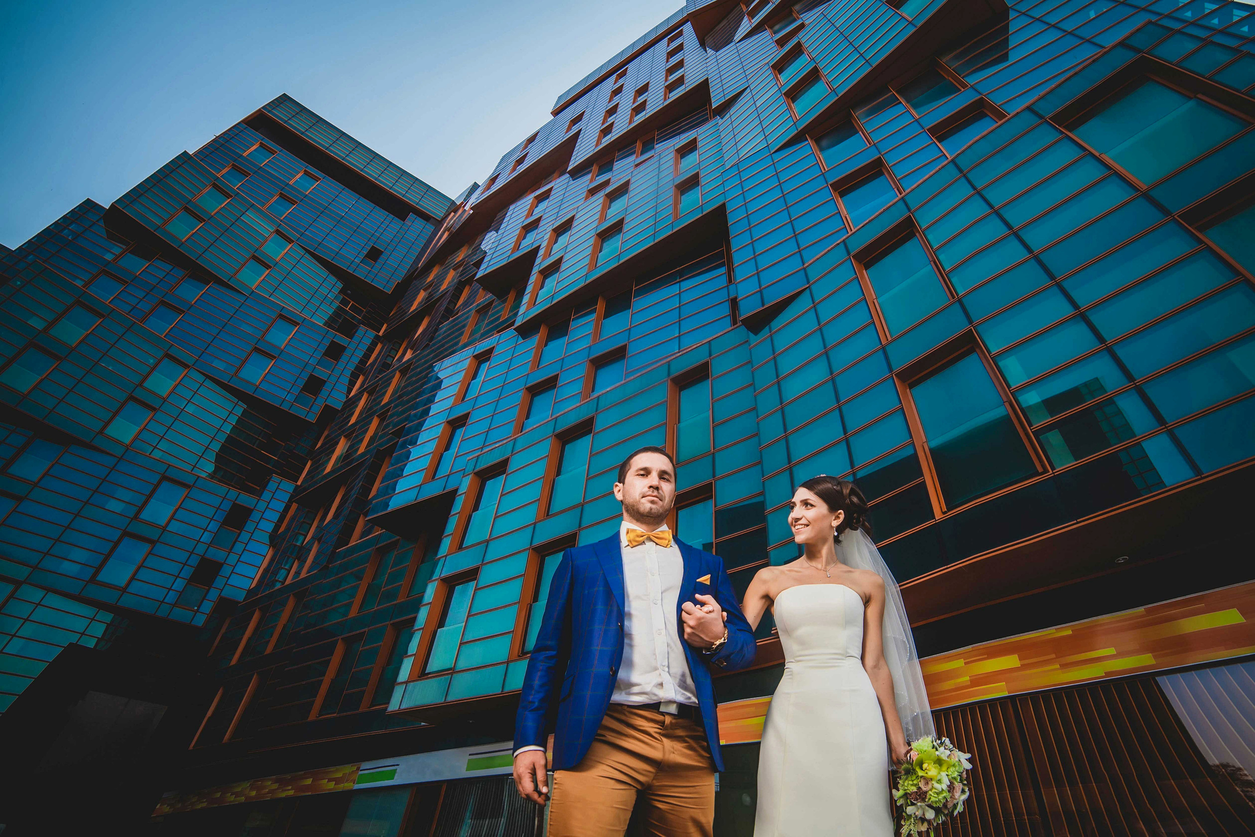 Жених и невеста стоят взявшись за куки на фоне высокого красивого здания