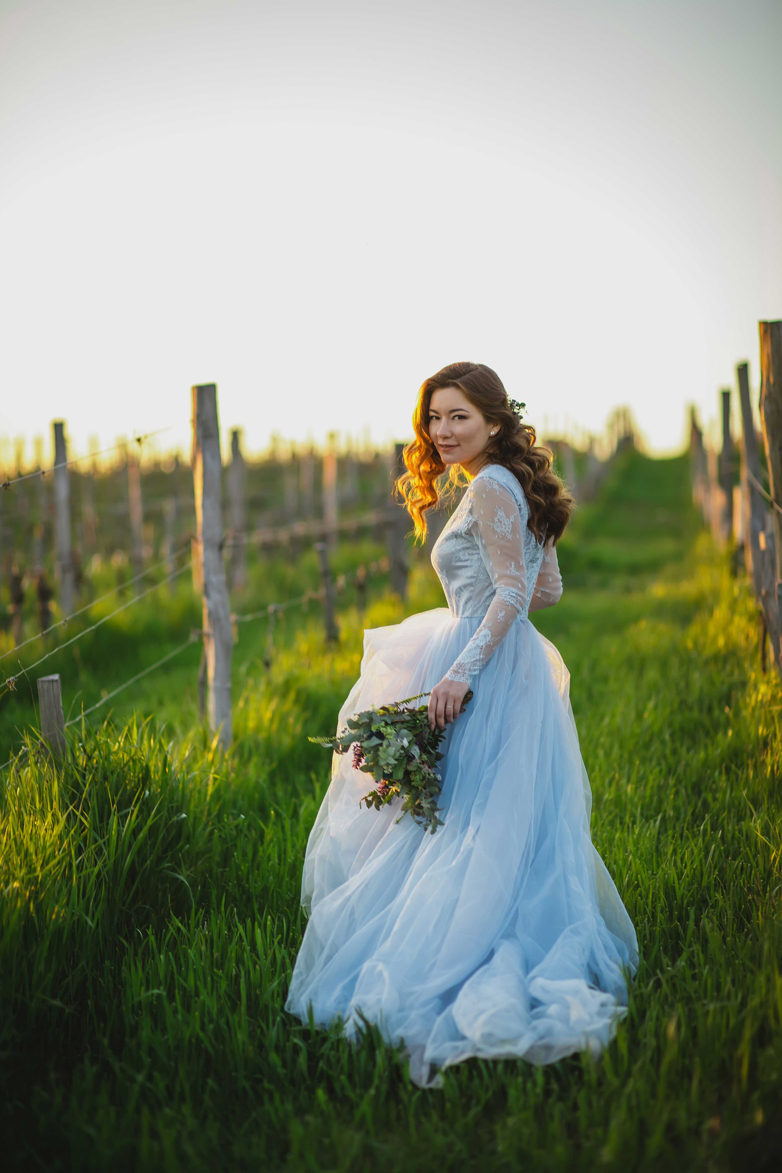 Красивая невеста в голубом свадебном платье с растрепанным свадебным букетом в виноградниках