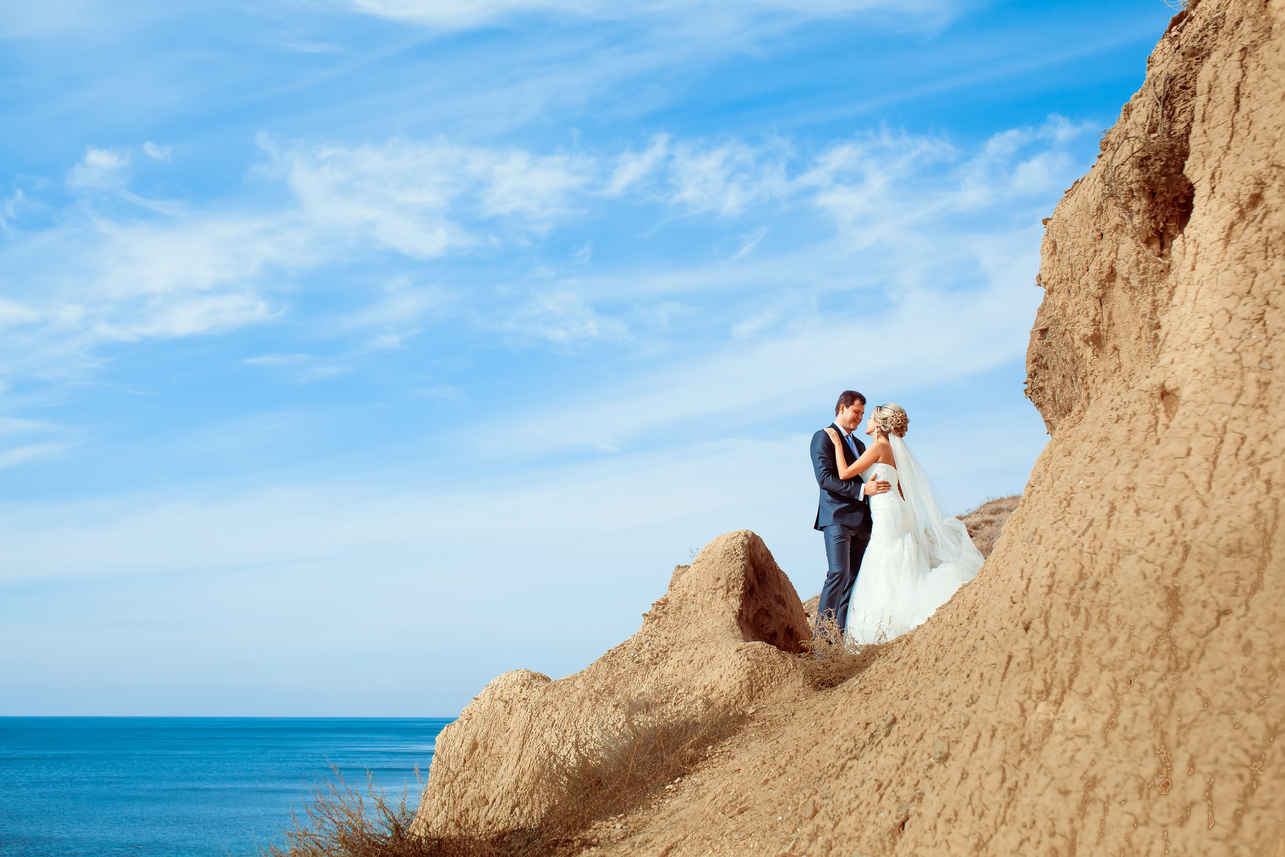 Жених и невеста стоят на фоне моря обнявшись