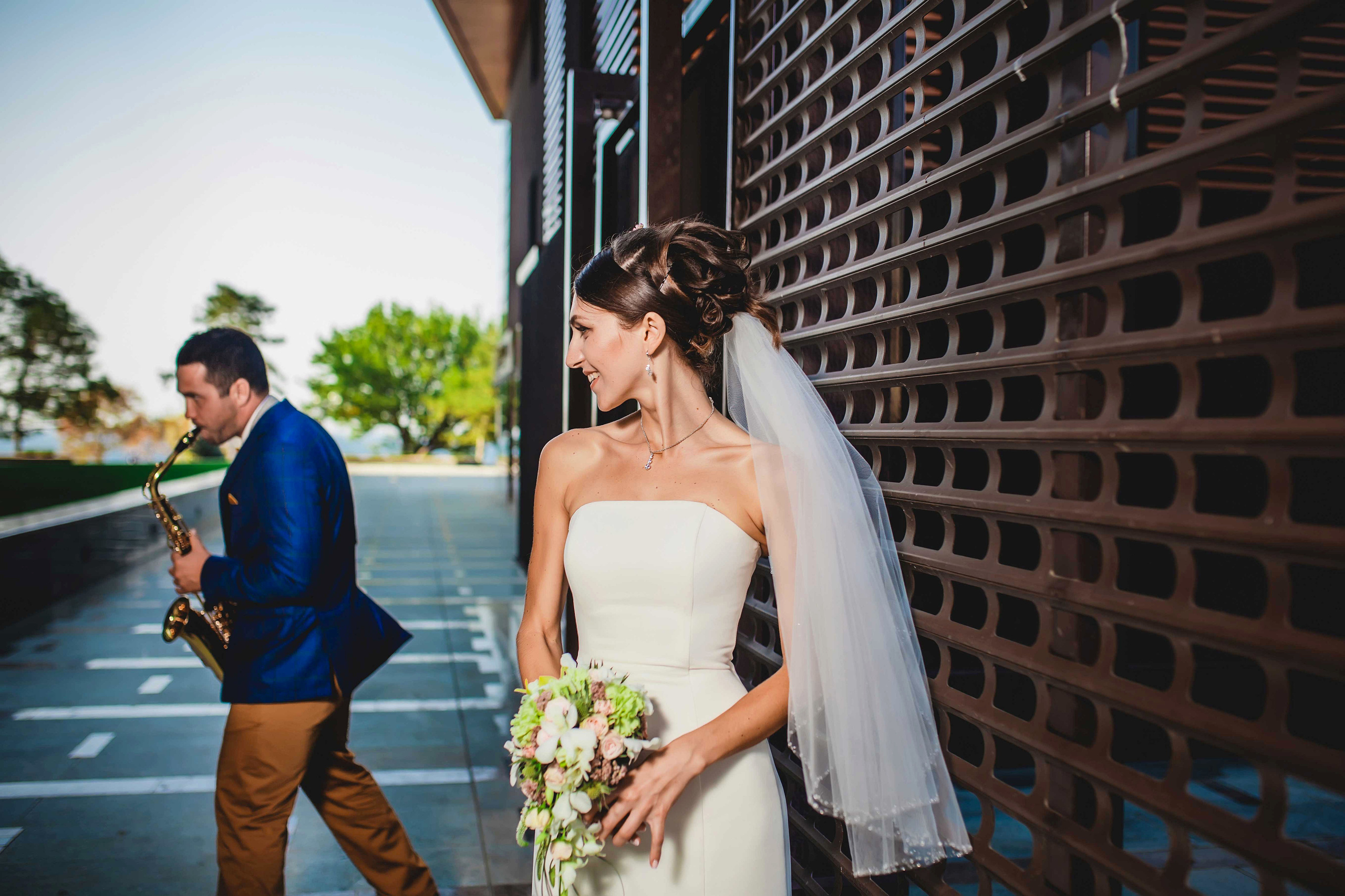 Жених играет на саксофоне а невеста  улыбаясь стоит рядом 