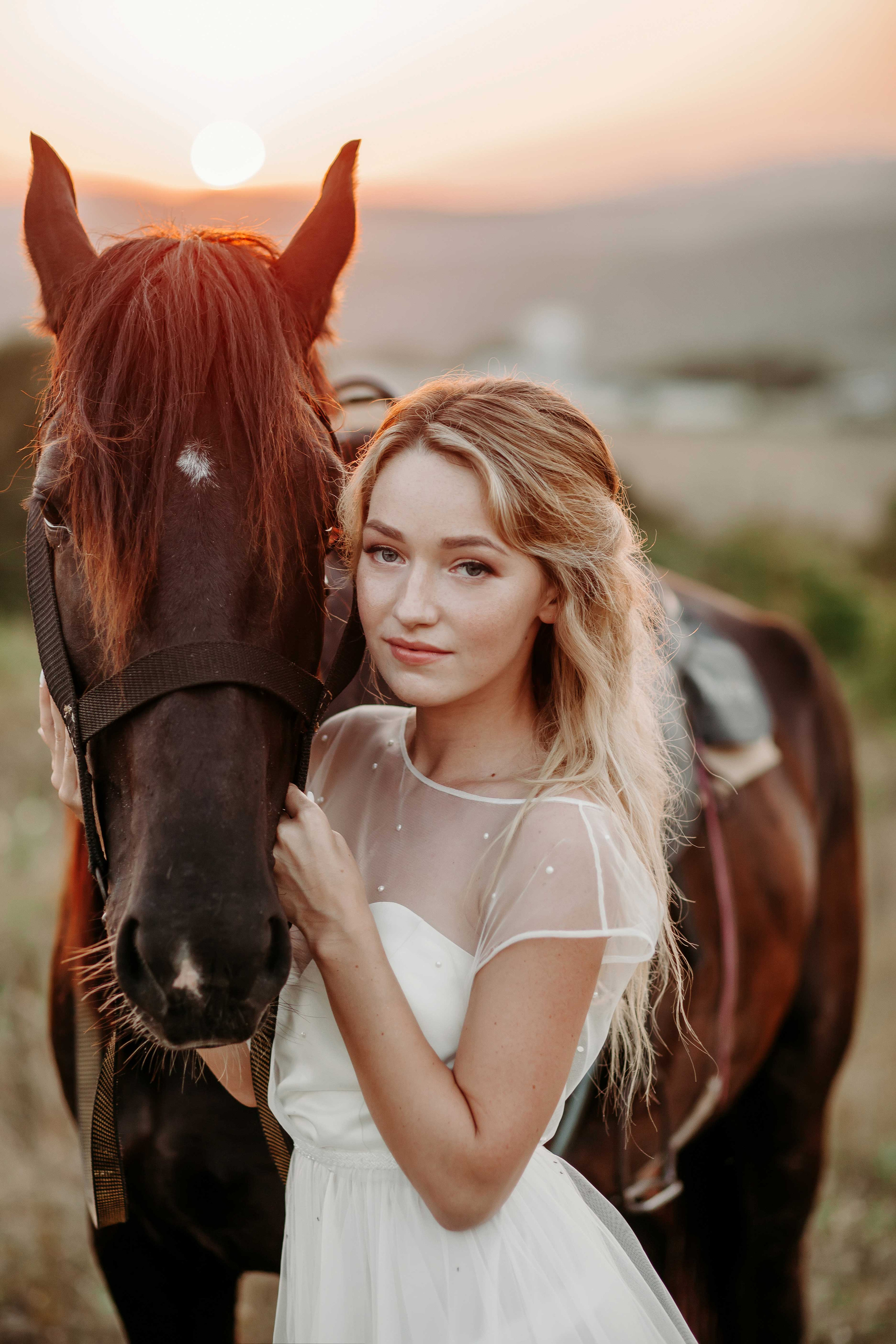Блондинка невеста в белом платье стоит рядом с лошадью