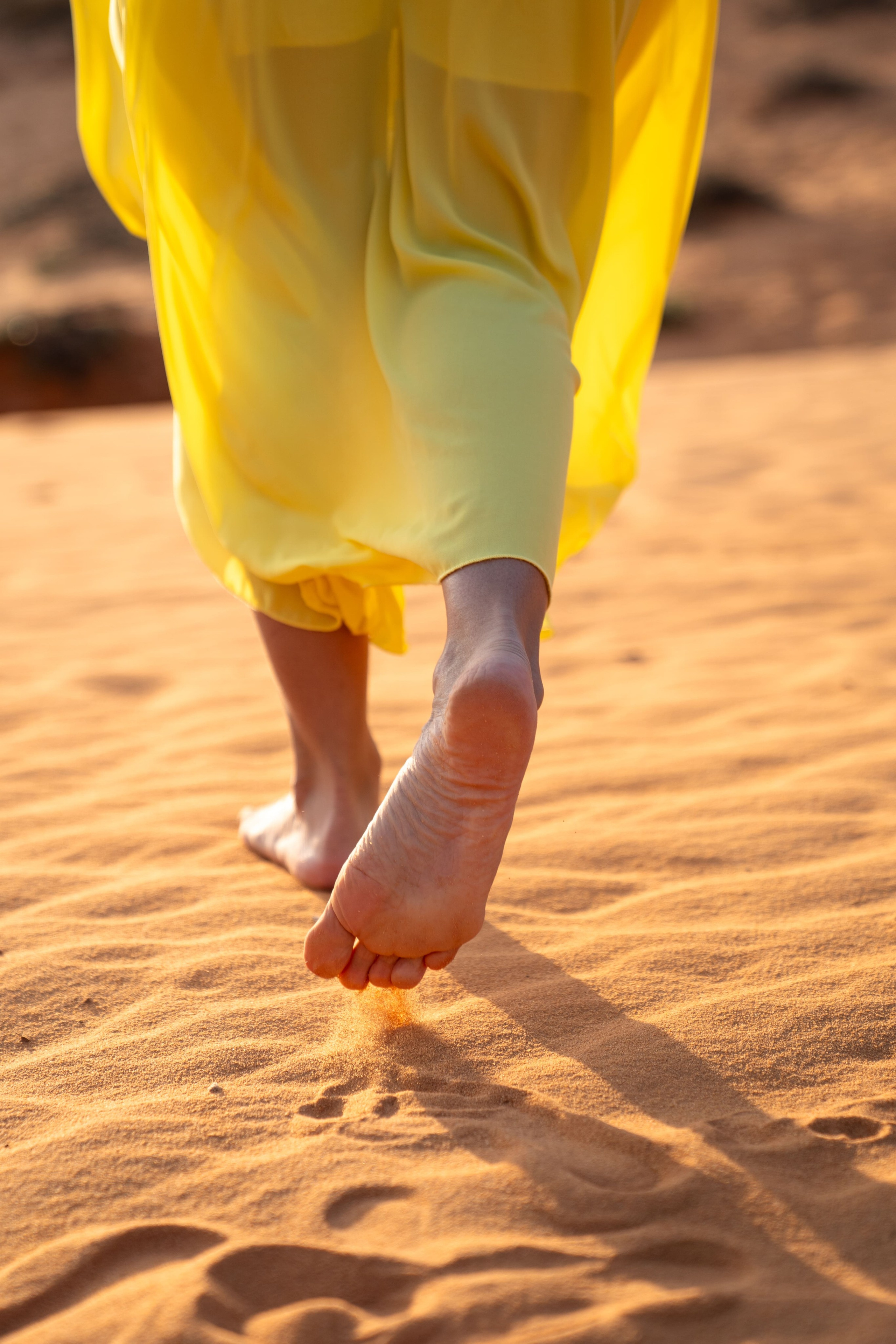 Крупный план босых ног в желтом платье, идущих по оранжевому песку пустыни на закате, атмосферный кадр Kartashow