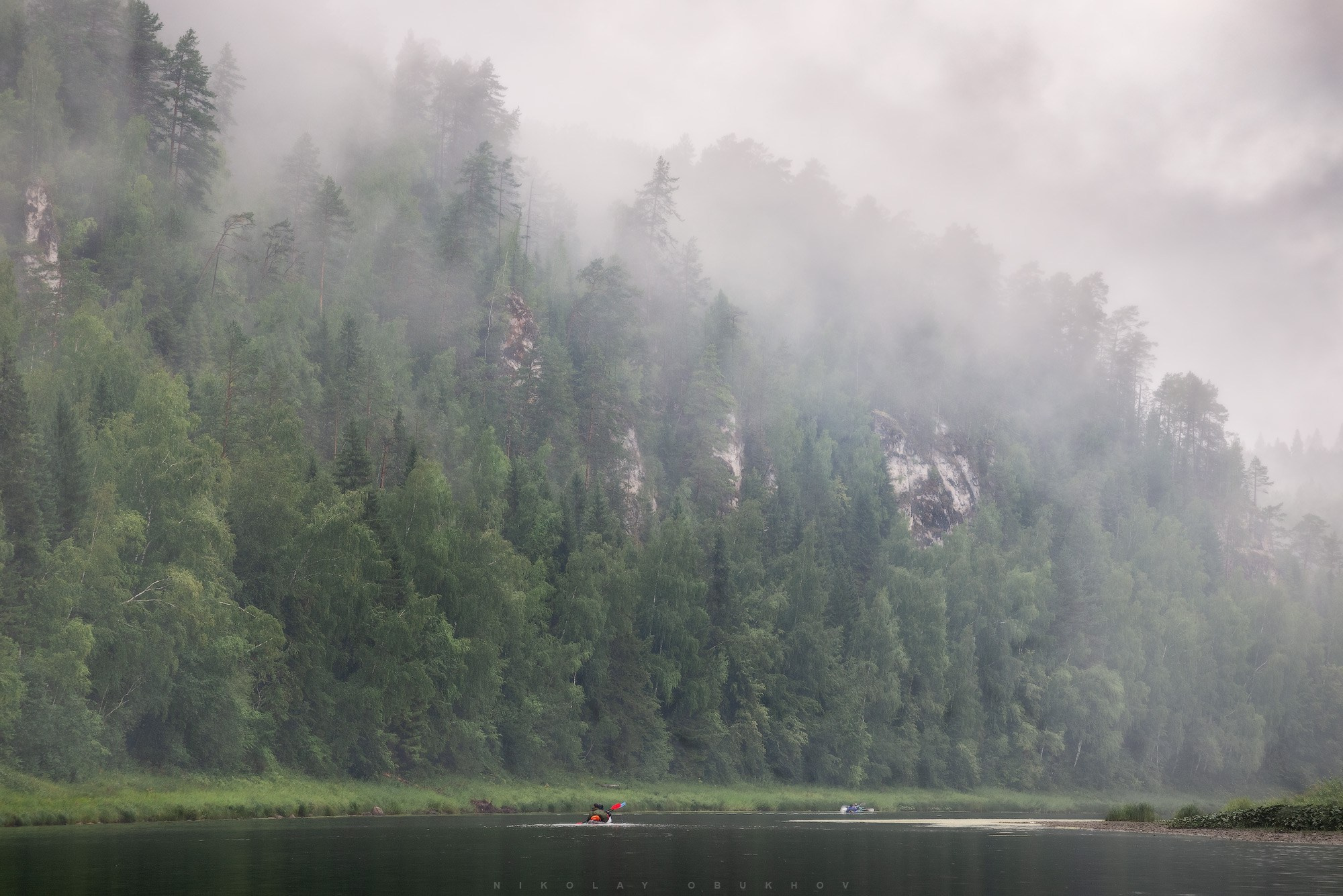 Байдарка плывет по реке во время сплава по реке Чусовая, скалы просвечивают сквозь туман после летного дождя