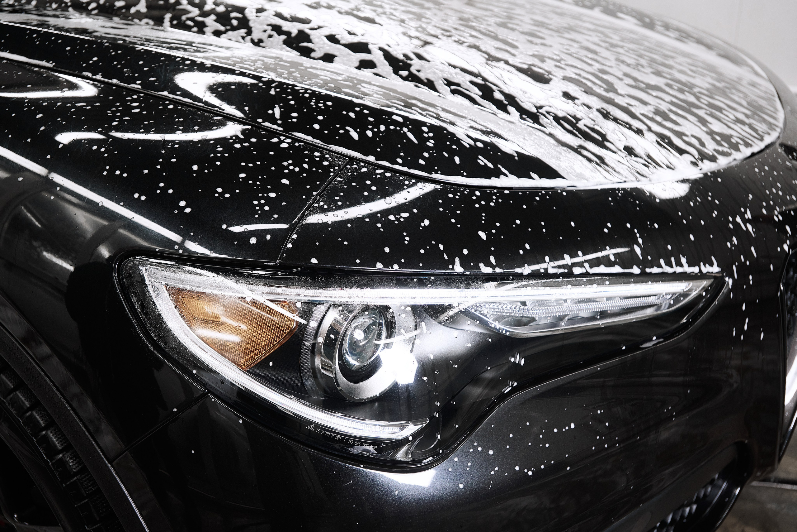 Крупный план передней фары Alfa Romeo Stelvio с пеной на кузове