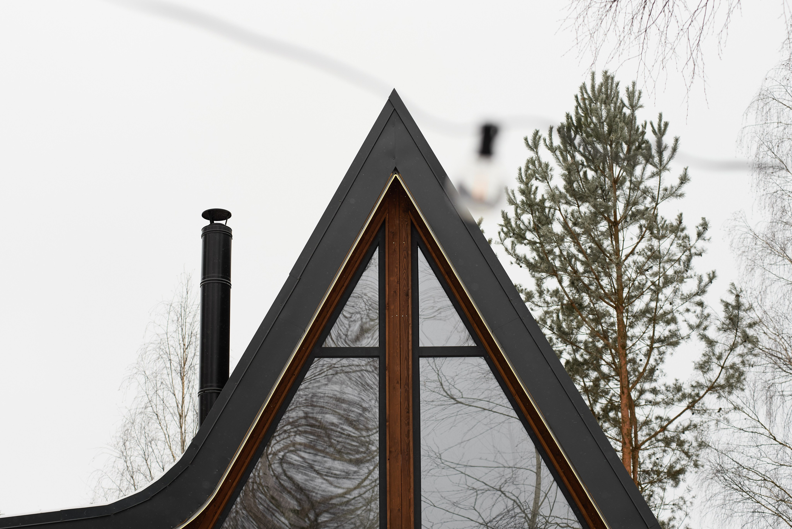 Фотосъёмка фронтона A-frame дома с высоким панорамным остеклением и тёмной кровлей