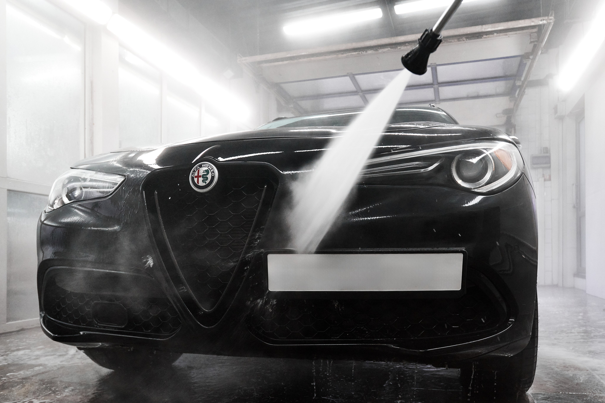 Фотосъёмка чёрного Alfa Romeo Stelvio спереди во время мойки аппаратом высокого давления