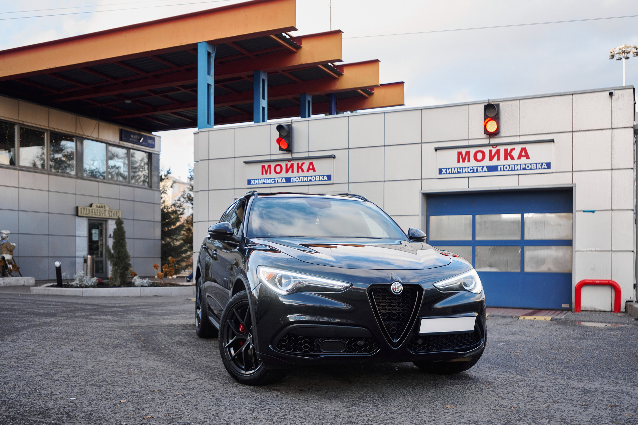 Фотосъёмка чёрного Alfa Romeo Stelvio возле автомойки в трёхчетвертном ракурсе