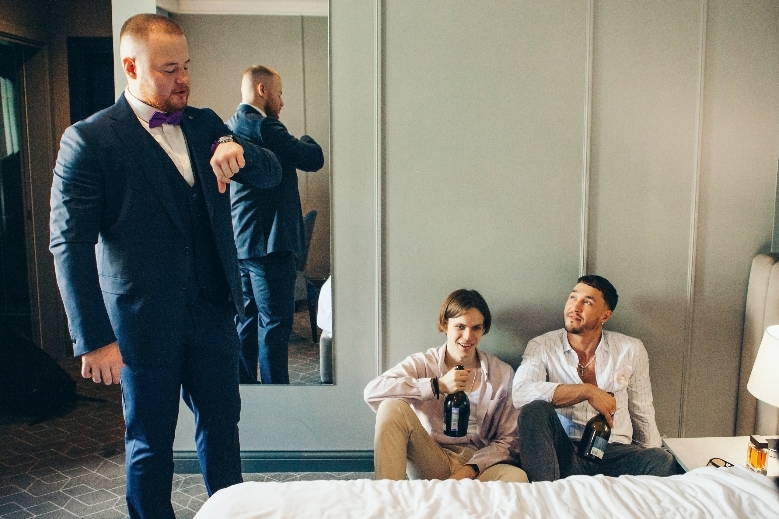 друзьях жениха сидят на полу и смотрят как их друг собирается на свадьбу