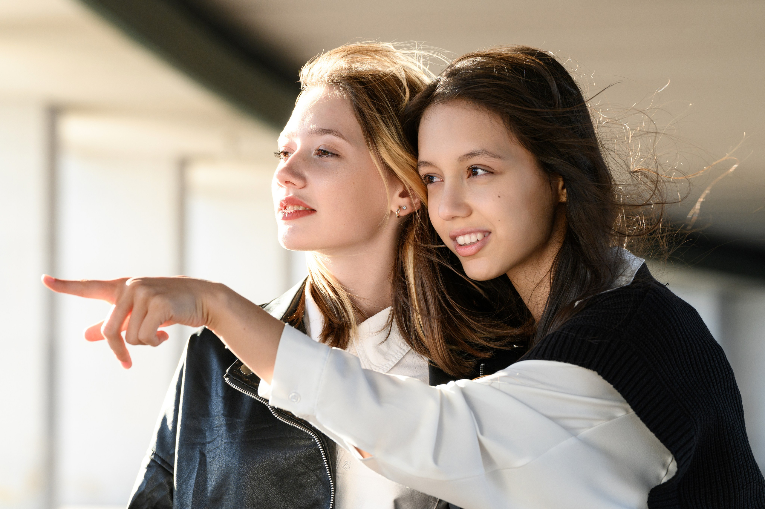 Две подруги обнимаются и смотрят вдаль в мягком естественном свете.