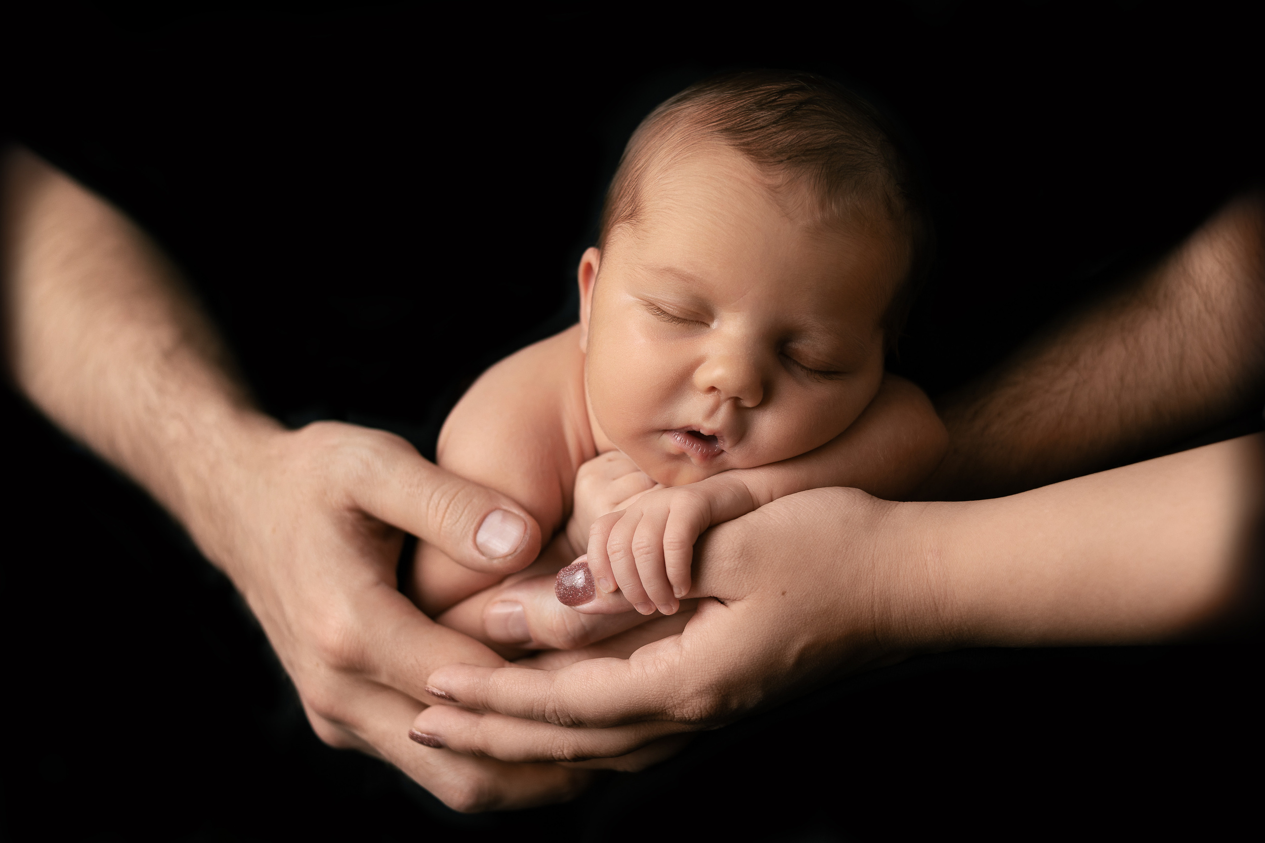 Младенец в руках мамы и папы на черном фоне