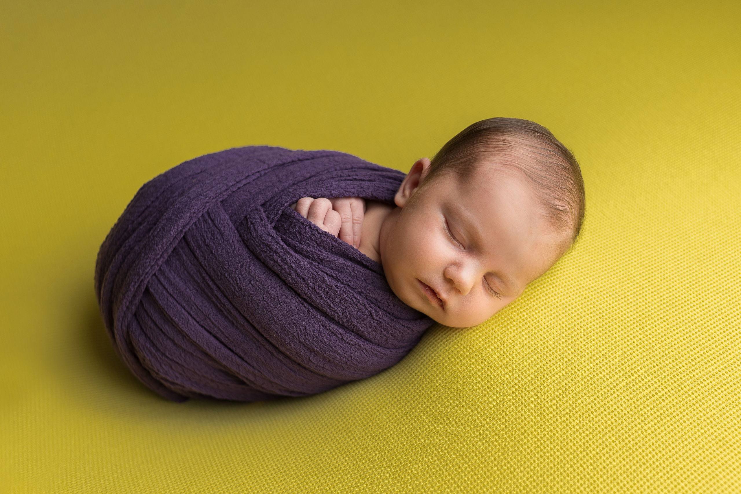 Ребенок в фиолетовом коконе на желтом фоне